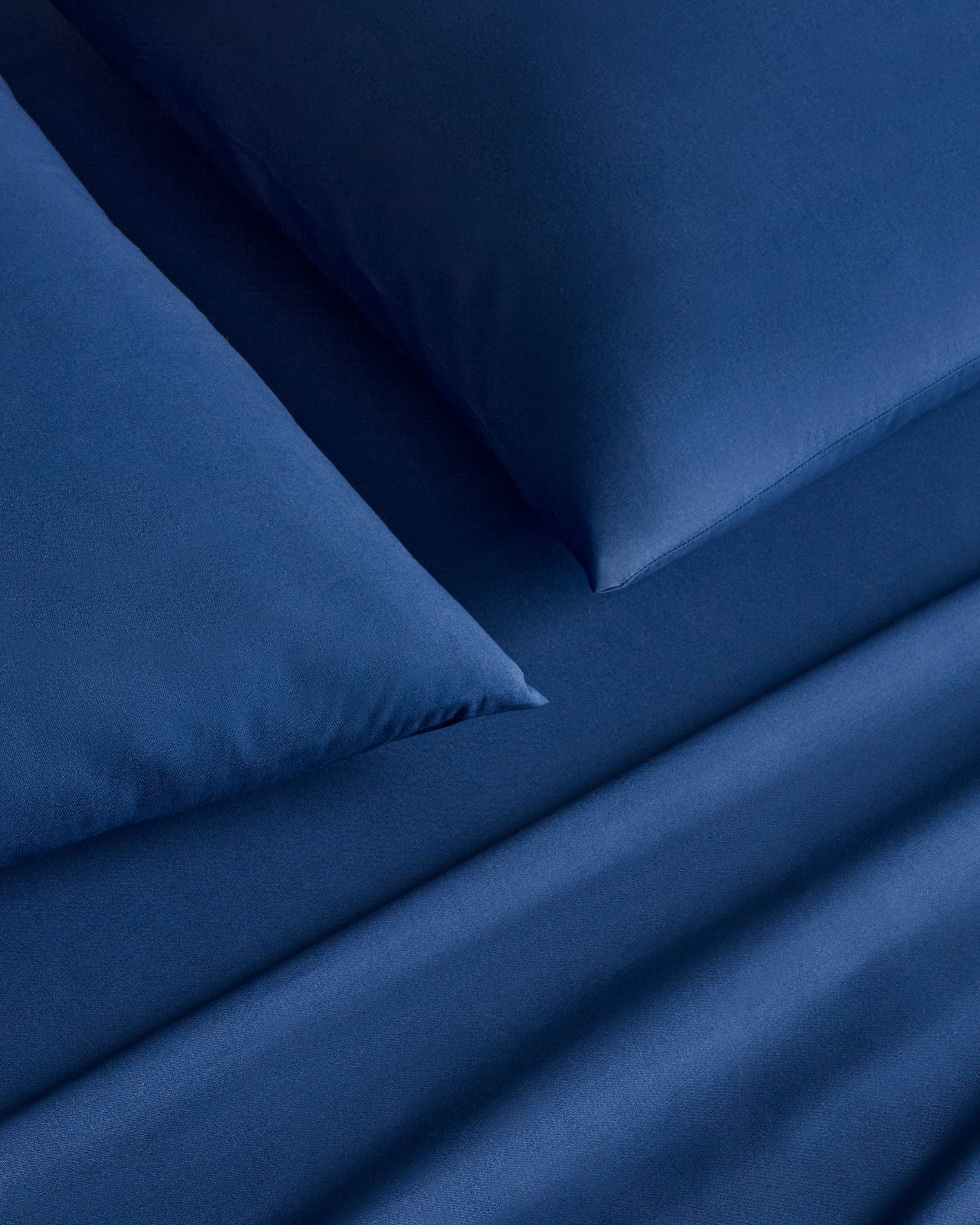 A close-up features a neatly made bed with Luxe Premium Cotton Bed Sheets in Navy by Petite Plume, showcasing silky long-staple cotton bedding and matching pillows for an opulent and calming look.
