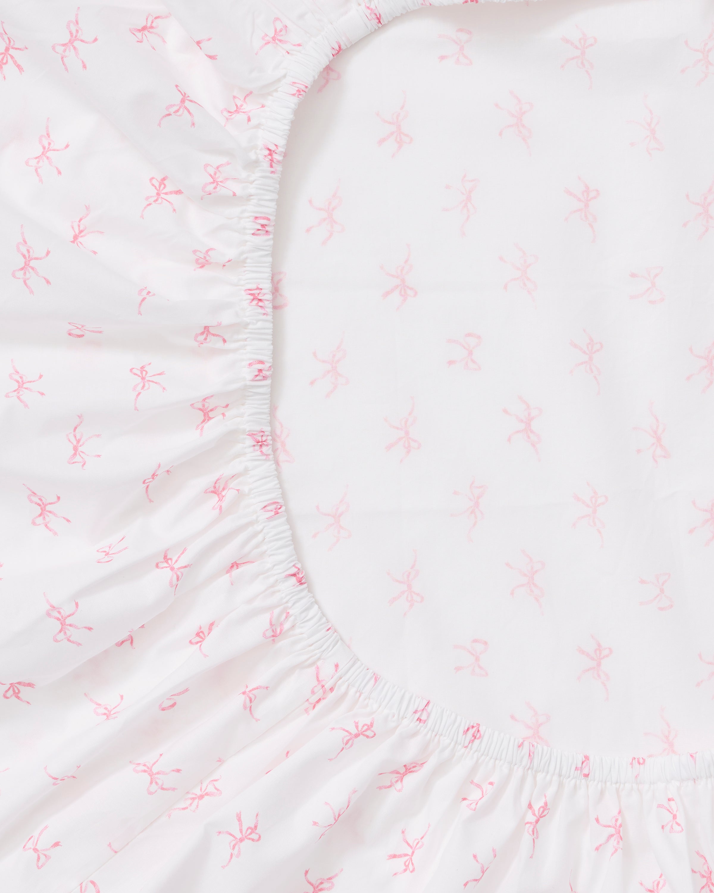 A close-up of the Luxe Premium Percale Crib Sheet in Blushing Bows, featuring a white background with a pattern of small pink ballerinas, neatly wrapped around the corner of a crib mattress.