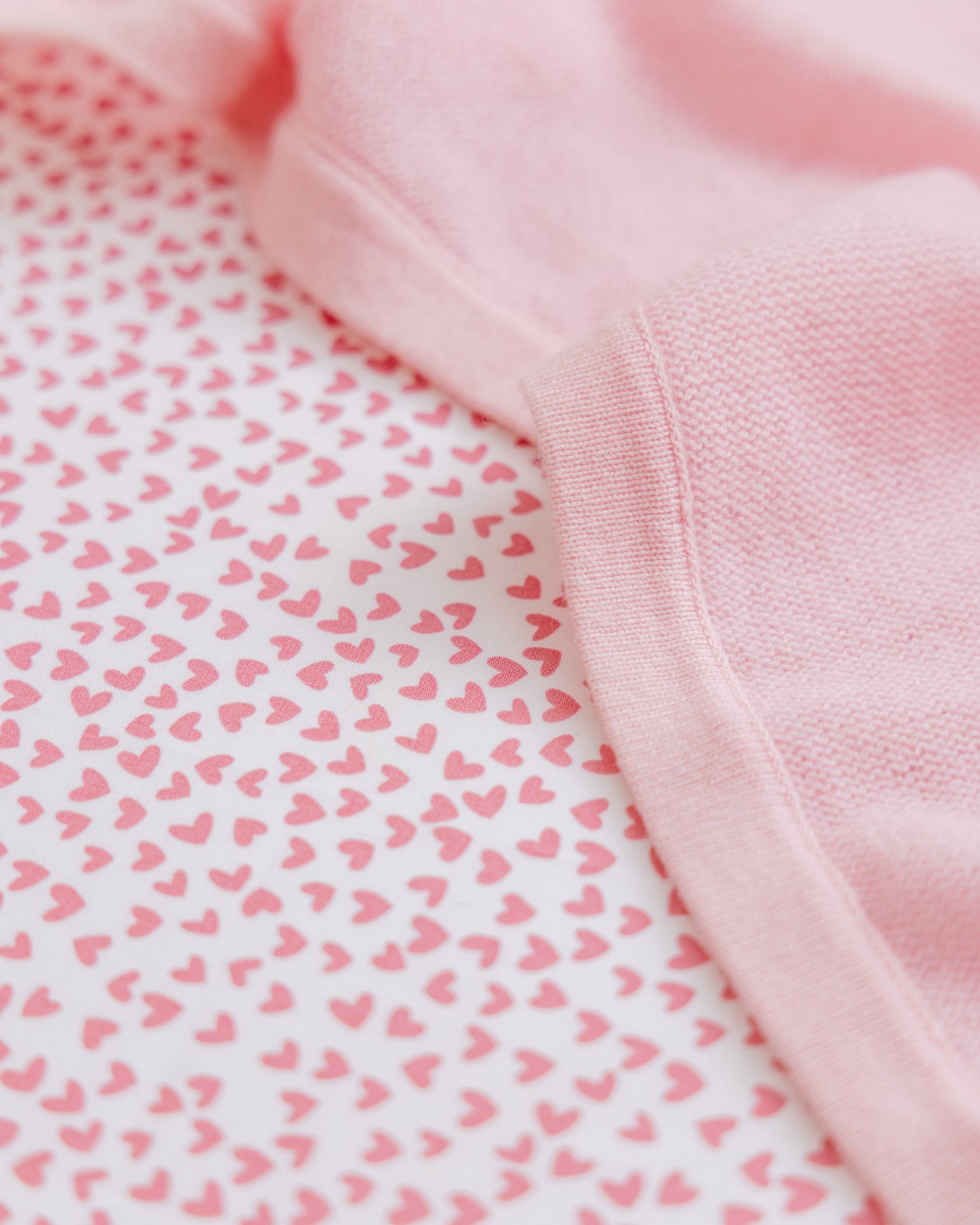 Close-up of a Luxe Premium Sweethearts Crib Sheet by Petite Plume, featuring a pink hue with a small heart pattern on a white background. Its ultra-soft, breathable fabric adds a cute and gentle touch.