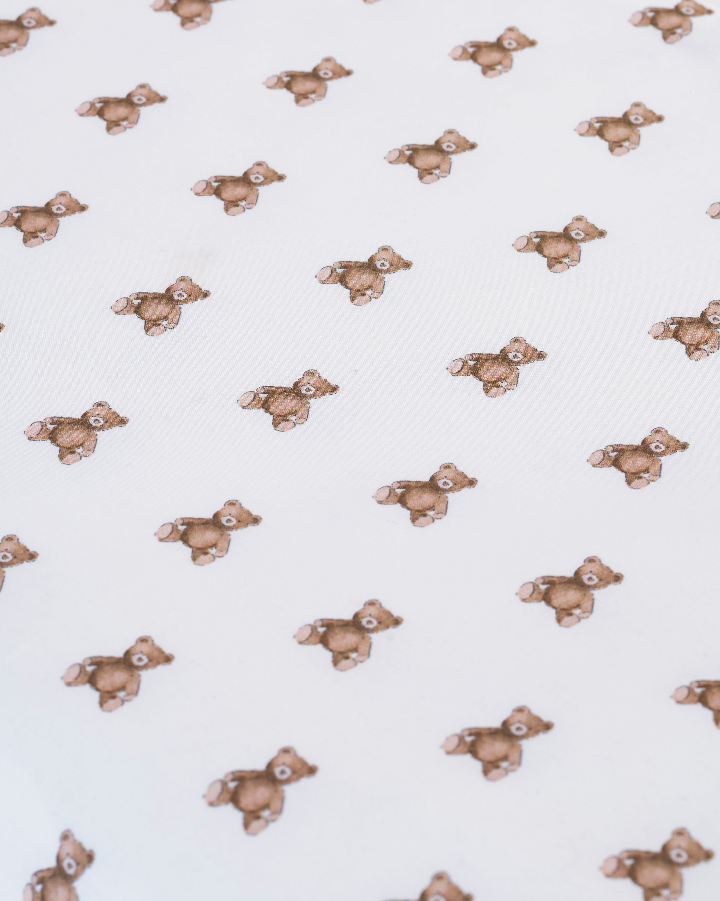 A stack of Luxe Premium Percale Bed Sheets in Teddy Tales, white and neatly folded, showcases a charming repeating pattern of small brown teddy bears.