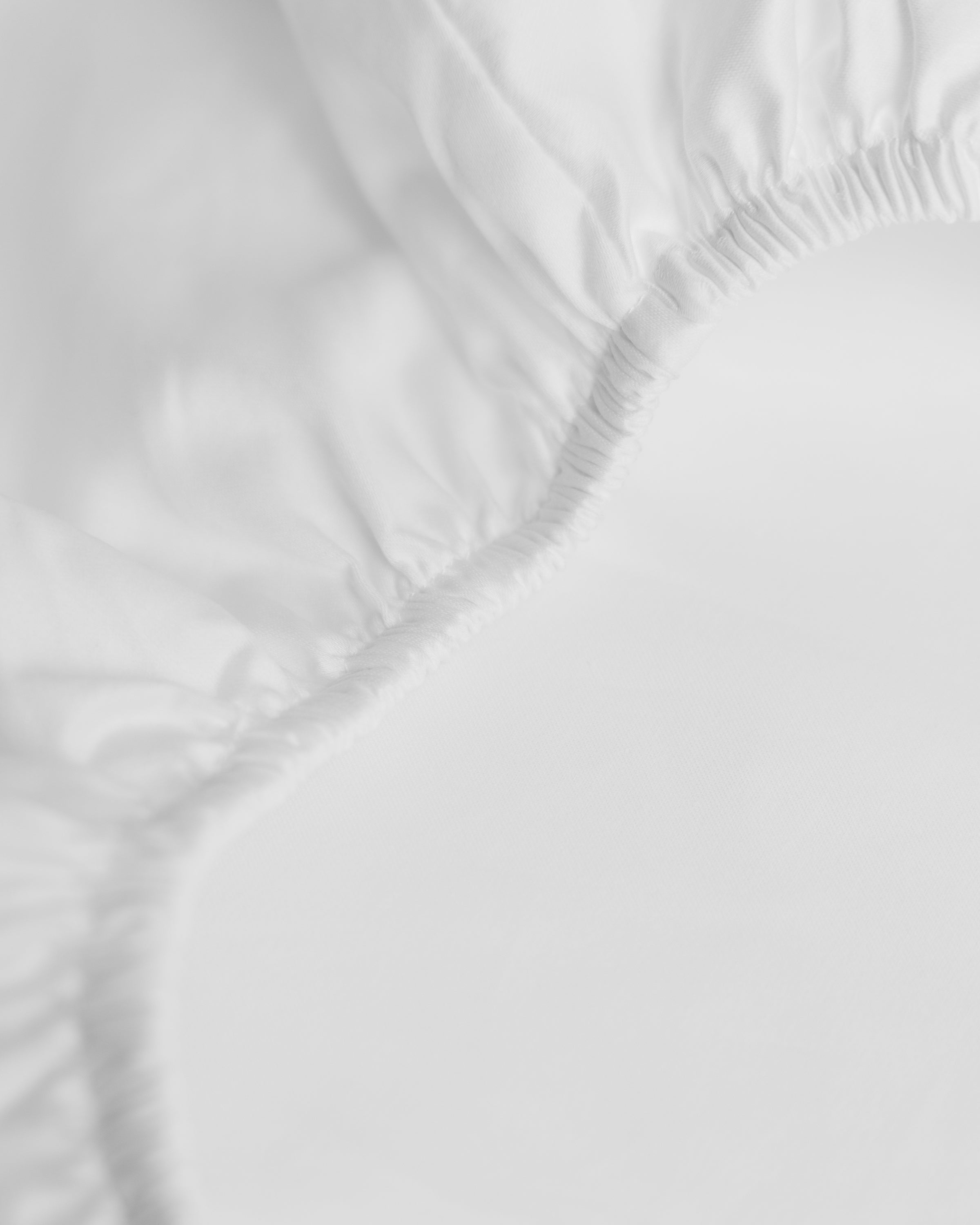 Close-up of Petite Plumes Signature Luxe Sateen Crib Sheet in White, highlighting the smooth, textured fabric and gathered corner with elastic edges. Made from long-staple cotton, the sateen weave enhances its crisp appearance under bright lighting.