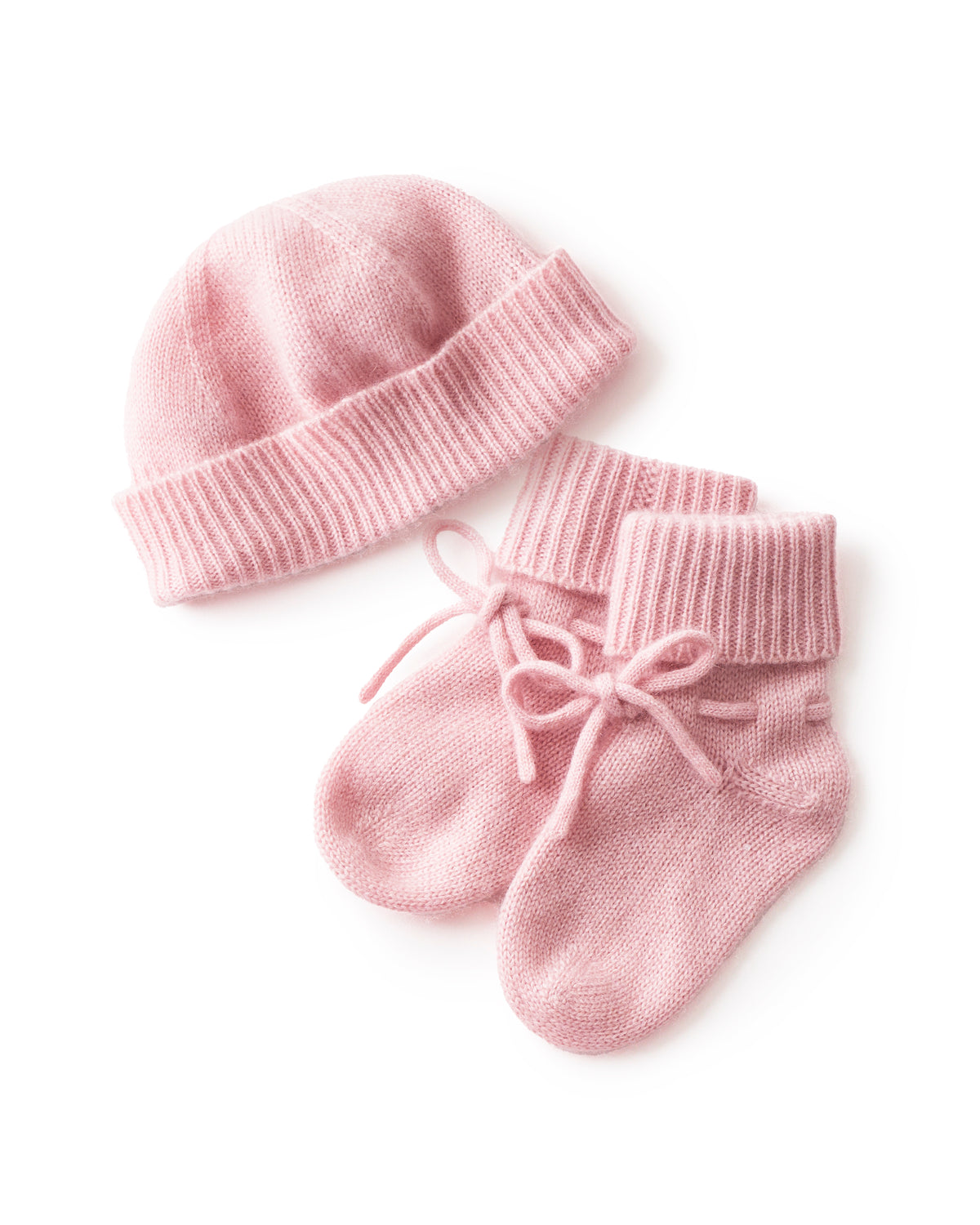 The Baby Cashmere Bootie & Hat Set in Rose features a pink knitted baby hat and matching booties with folded cuffs and tied laces, displayed on a white background.