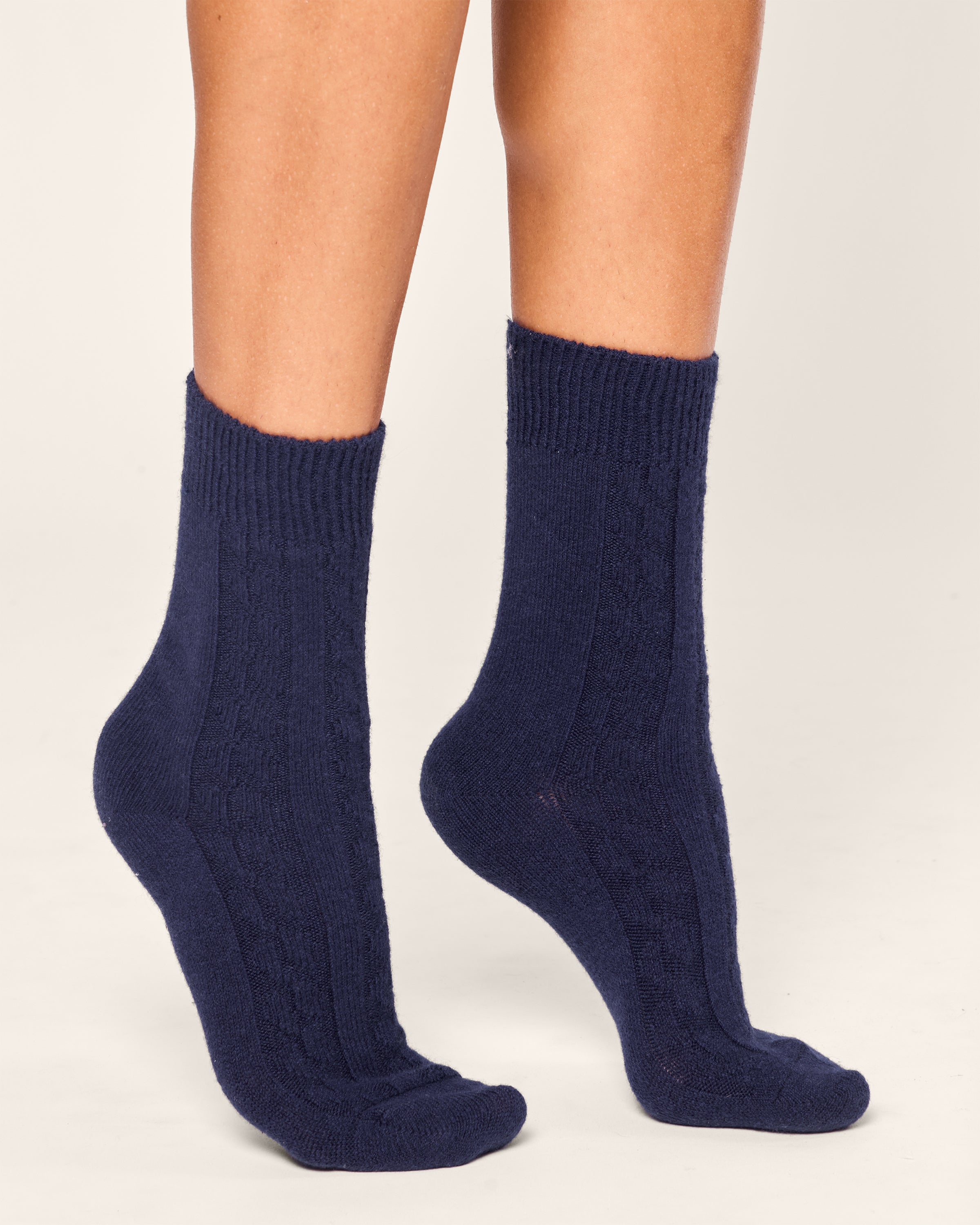 A close-up shows a person wearing Petite Plume Womens Cashmere Socks in Navy, standing with one foot slightly ahead of the other, exuding luxurious comfort against a plain white background.