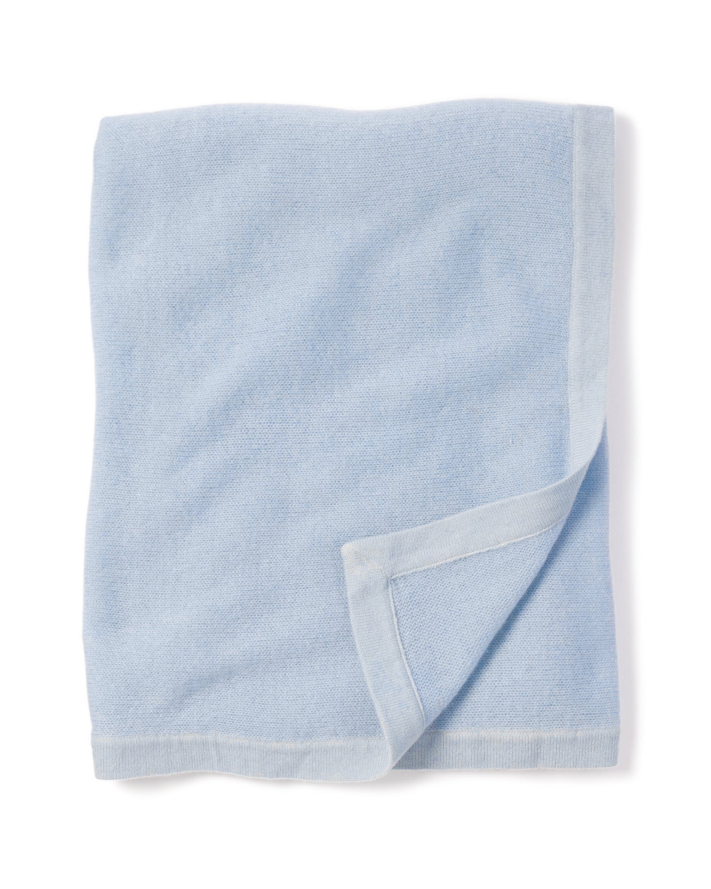 A neatly folded Cashmere Baby Blanket in Indigo by Petite Plume, with a luxuriously soft texture. The bottom right corner is slightly turned up, showcasing the underside. Edges are bordered with a darker indigo shade, evoking the elegance of a luxury baby gift.