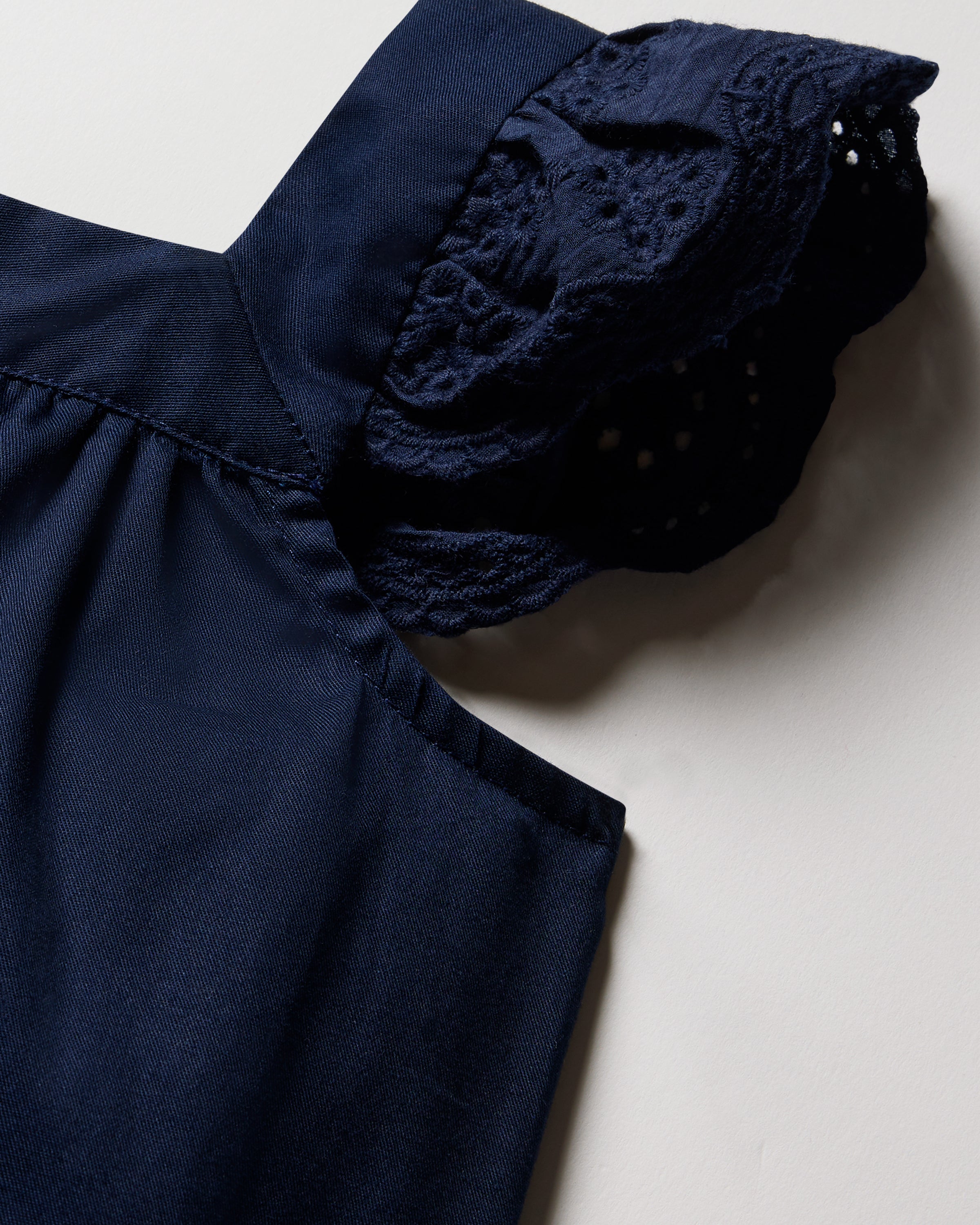 Close-up of Petite Plumes Girls Twill Clara Short Set in Navy, featuring sleeveless lace details on the shoulders. Made from premium cotton with a smooth texture, the intricate lace adds elegance. The set is displayed flat on a light-colored surface.