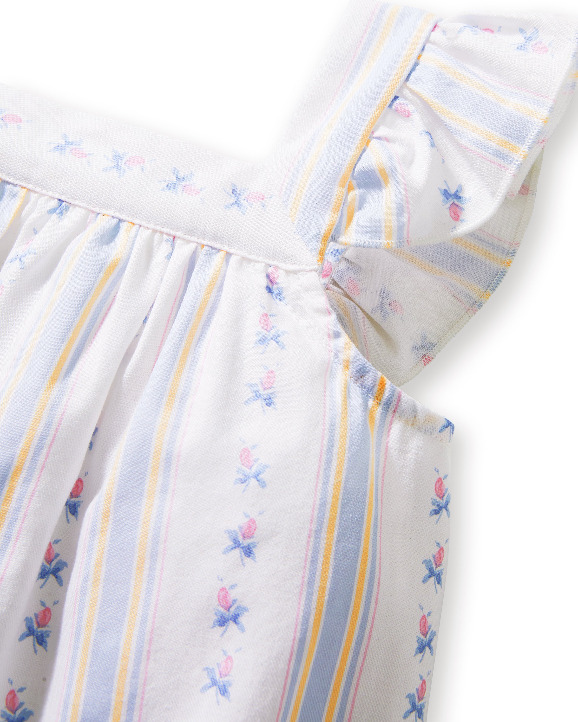 A young girl with curly hair smiles barefoot, wearing the Girl's Twill Clara Short Set in Cottage Stripe— a white sleeveless nightgown and matching shorts—against a plain, light background.