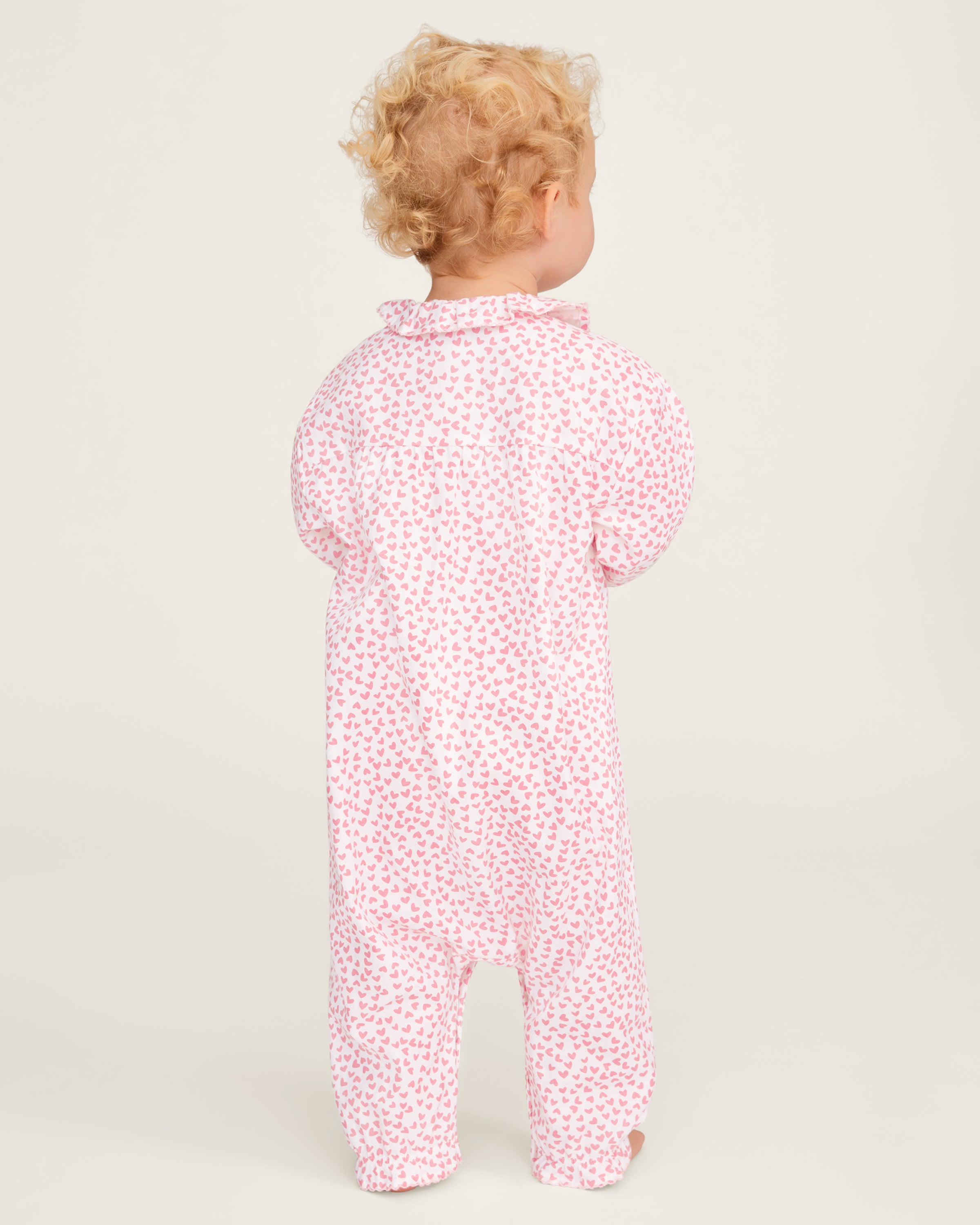 The Baby's Twill Madeline Romper in Sweethearts is a pink and white long-sleeve romper featuring a ruffled collar and cuffs, adorned with a small pink heart pattern.