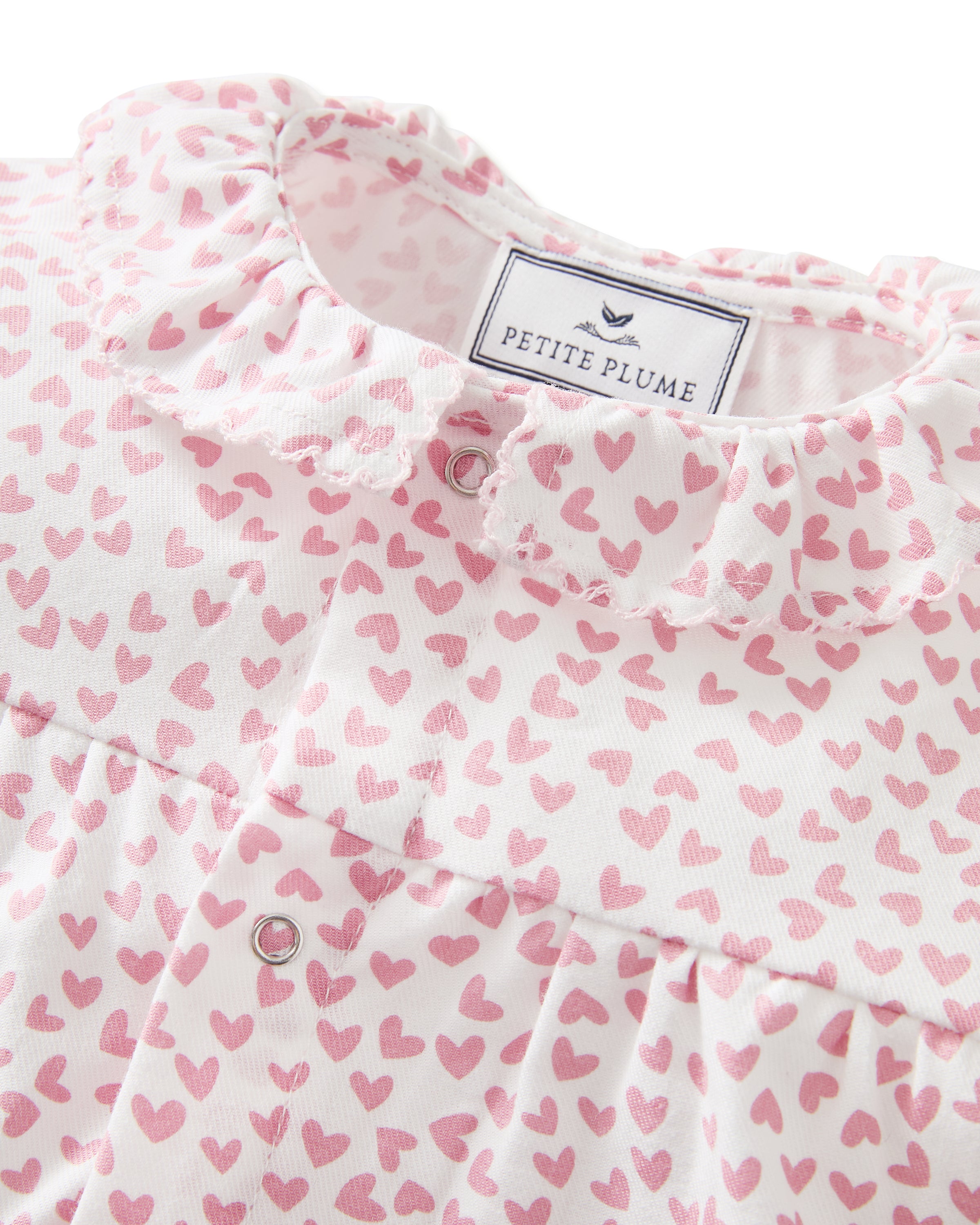 The Baby's Twill Madeline Romper in Sweethearts is a pink and white long-sleeve romper featuring a ruffled collar and cuffs, adorned with a small pink heart pattern.