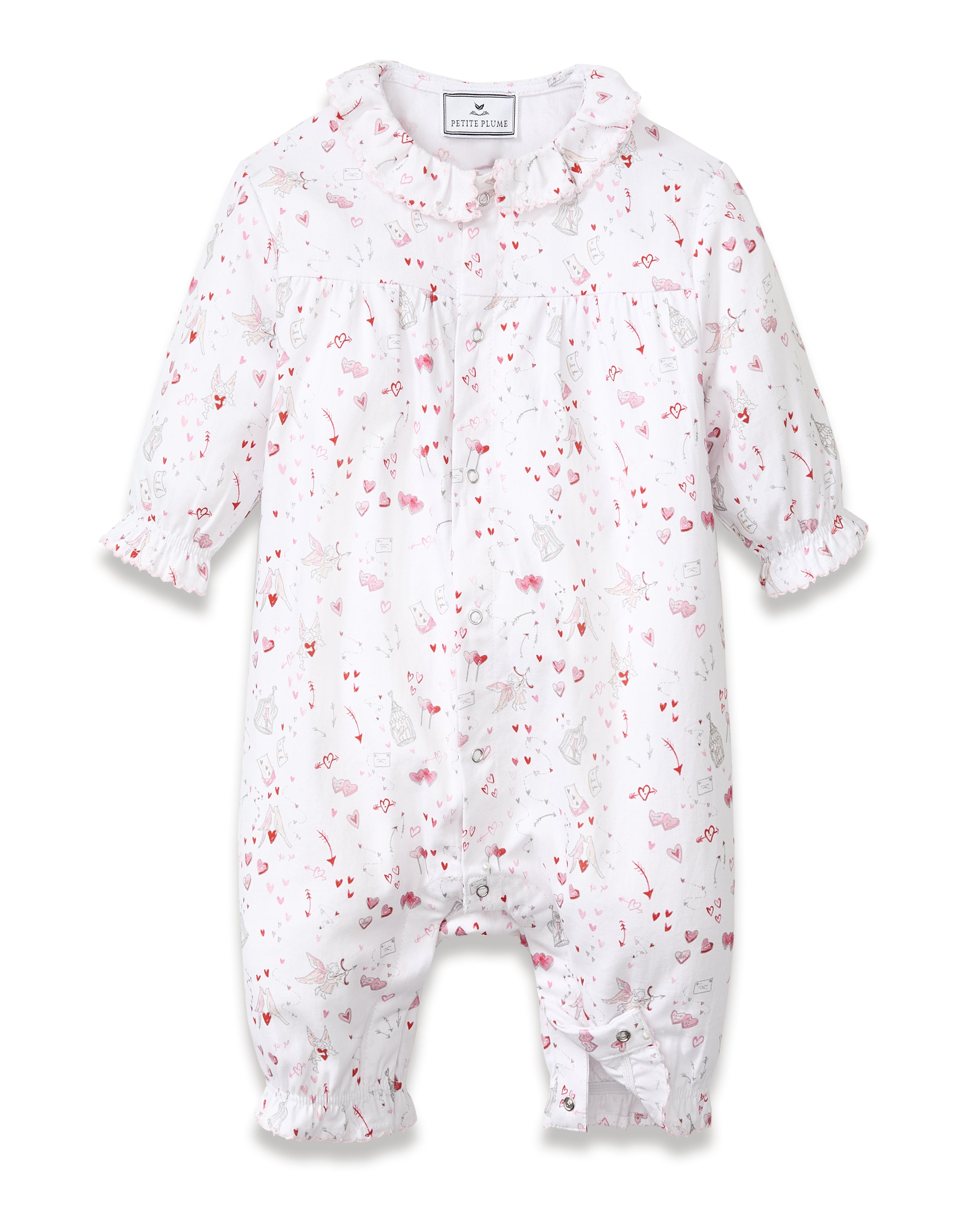 The Baby's Twill Madeline Romper in Love Song is a white long-sleeve romper with ruffled cuffs and collar, decorated with a pink pattern of hearts, glasses, and small animals. It features snap buttons down the front and legs.