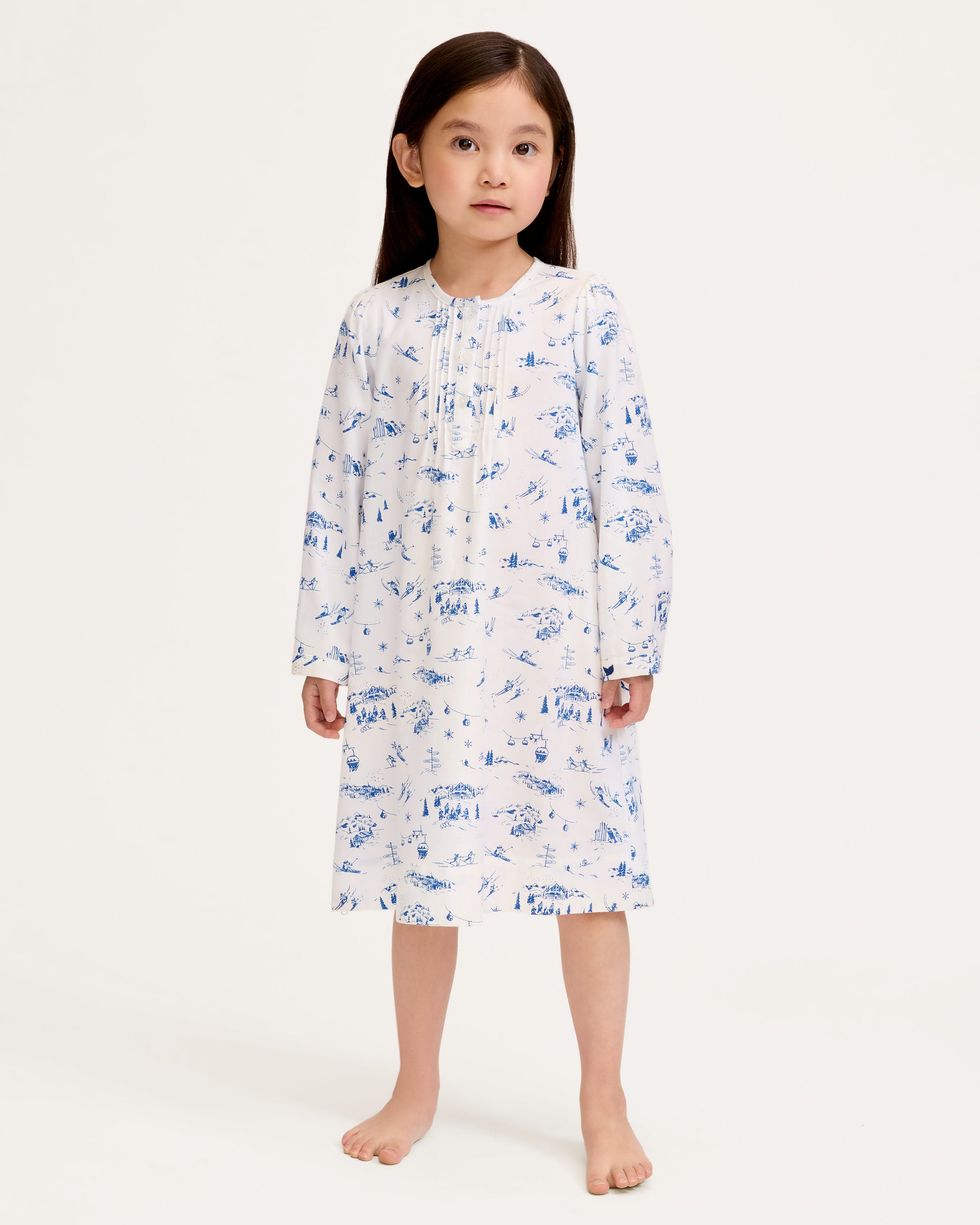 The Girl's Twill Beatrice Nightgown in Chalet Toile features long sleeves, knee-length, white fabric with blue scenic prints, a round neckline, pintucks on the chest, a loose fit, and button details at the neck.
