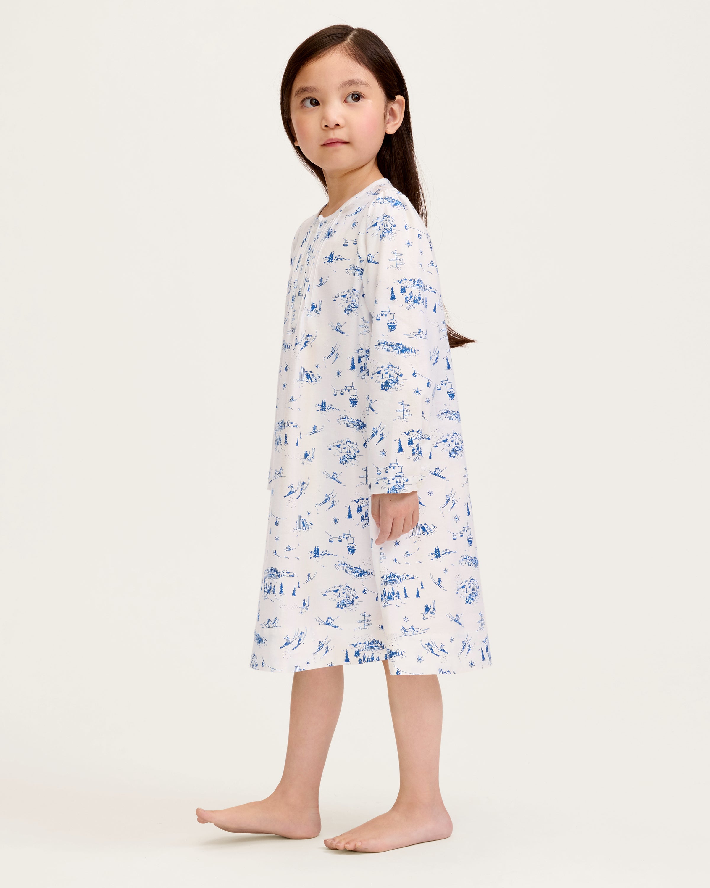 The Girl's Twill Beatrice Nightgown in Chalet Toile features long sleeves, knee-length, white fabric with blue scenic prints, a round neckline, pintucks on the chest, a loose fit, and button details at the neck.