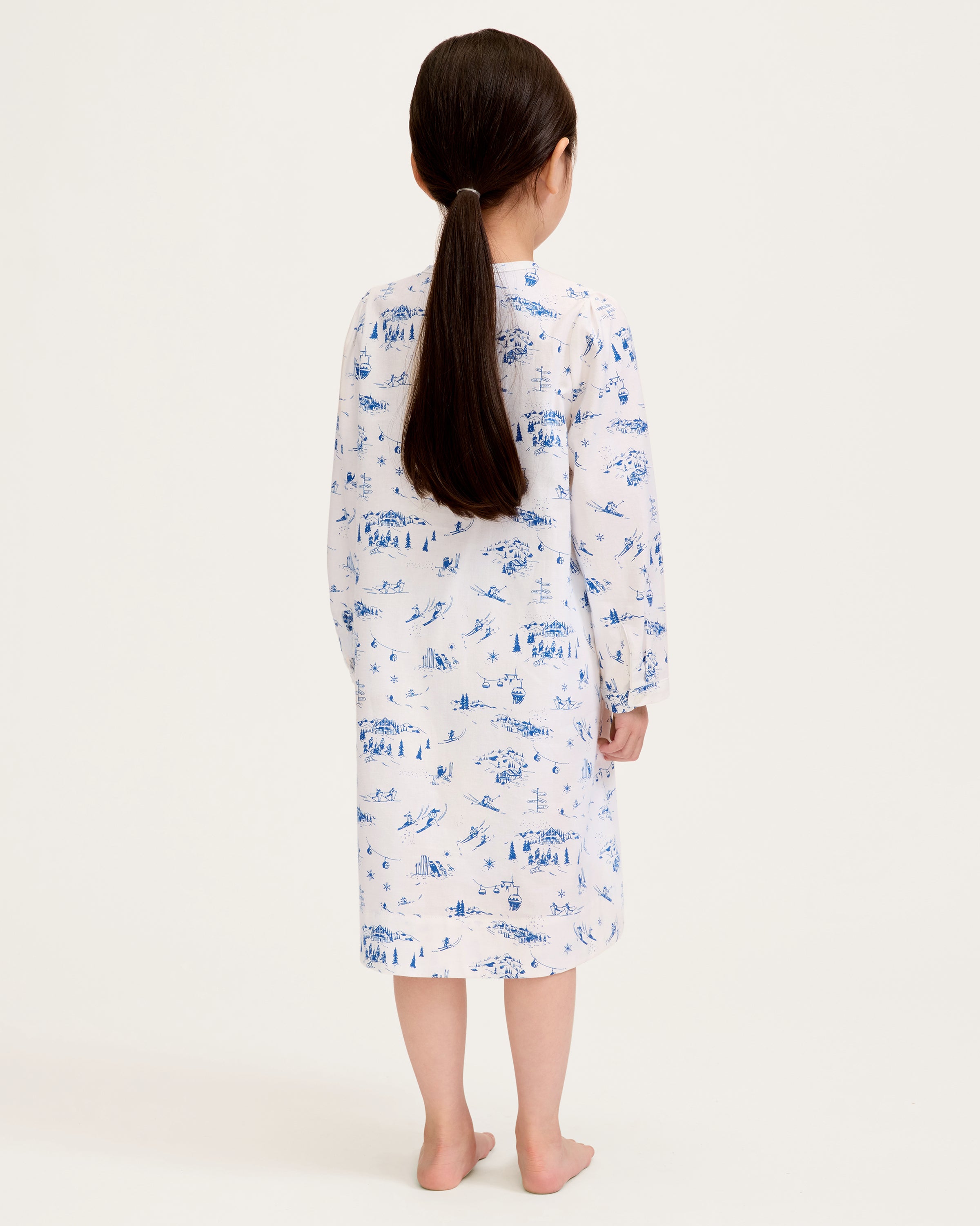 The Girl's Twill Beatrice Nightgown in Chalet Toile features long sleeves, knee-length, white fabric with blue scenic prints, a round neckline, pintucks on the chest, a loose fit, and button details at the neck.