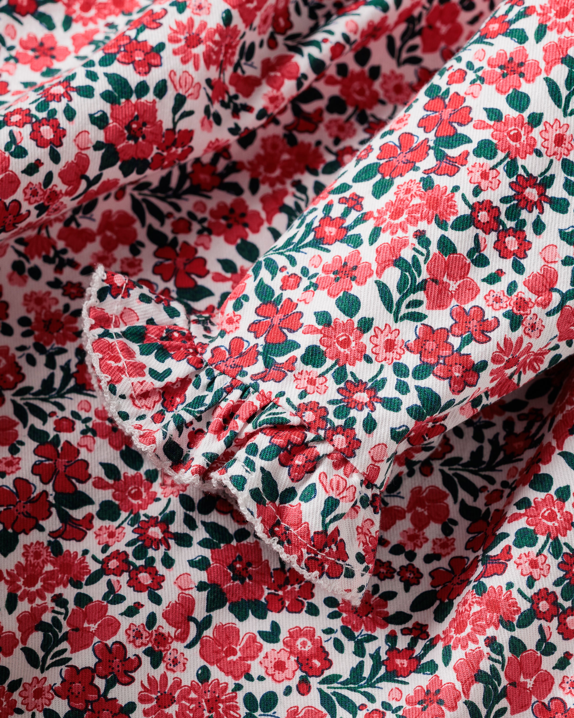 A detail of the Girls Eloise Nightgown in Fleurs des Bois by Petite Plume shows a vibrant red floral pattern with green leaves on white, complemented by frilled trim that enhances its textured surface and colorful design. Perfect for a floral print nightgown.