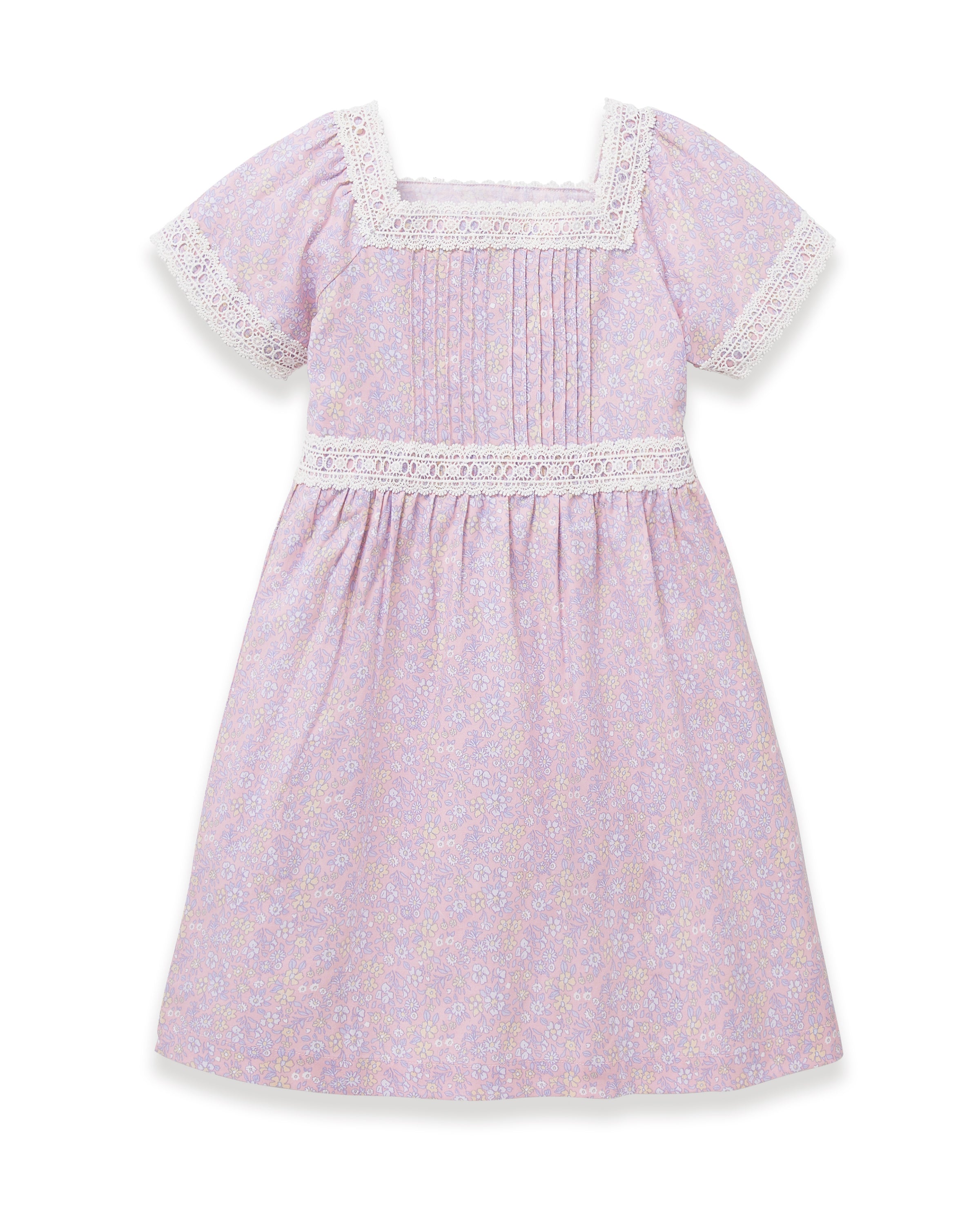 A young girl with long dark hair stands barefoot, wearing the Girl's Twill Juliette Nightgown in Fleur Blush—a light purple, knee-length dress featuring short sleeves, lace trim, and a delicate floral pattern—against a plain light background.
