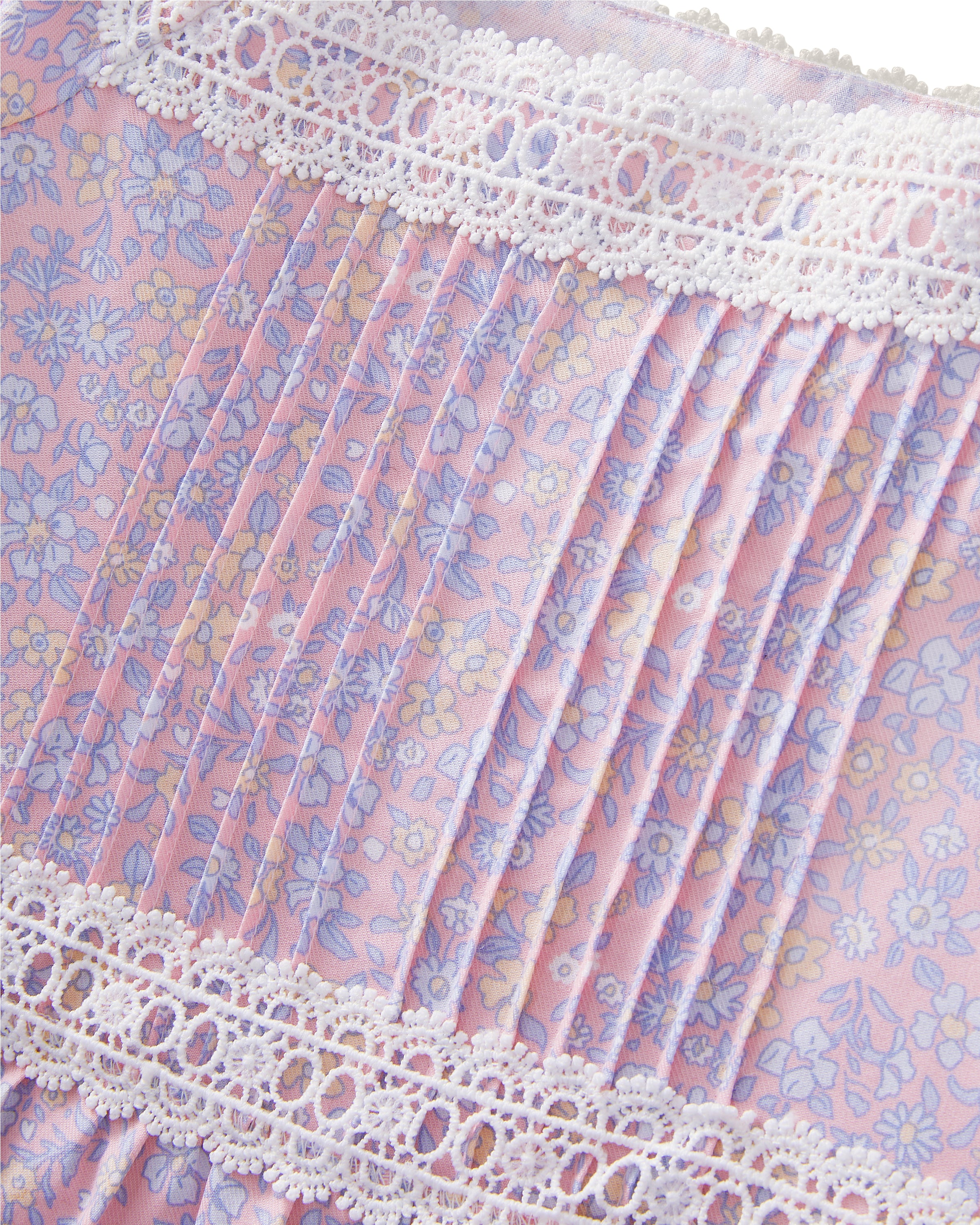 A young girl with long dark hair stands barefoot, wearing the Girl's Twill Juliette Nightgown in Fleur Blush—a light purple, knee-length dress featuring short sleeves, lace trim, and a delicate floral pattern—against a plain light background.