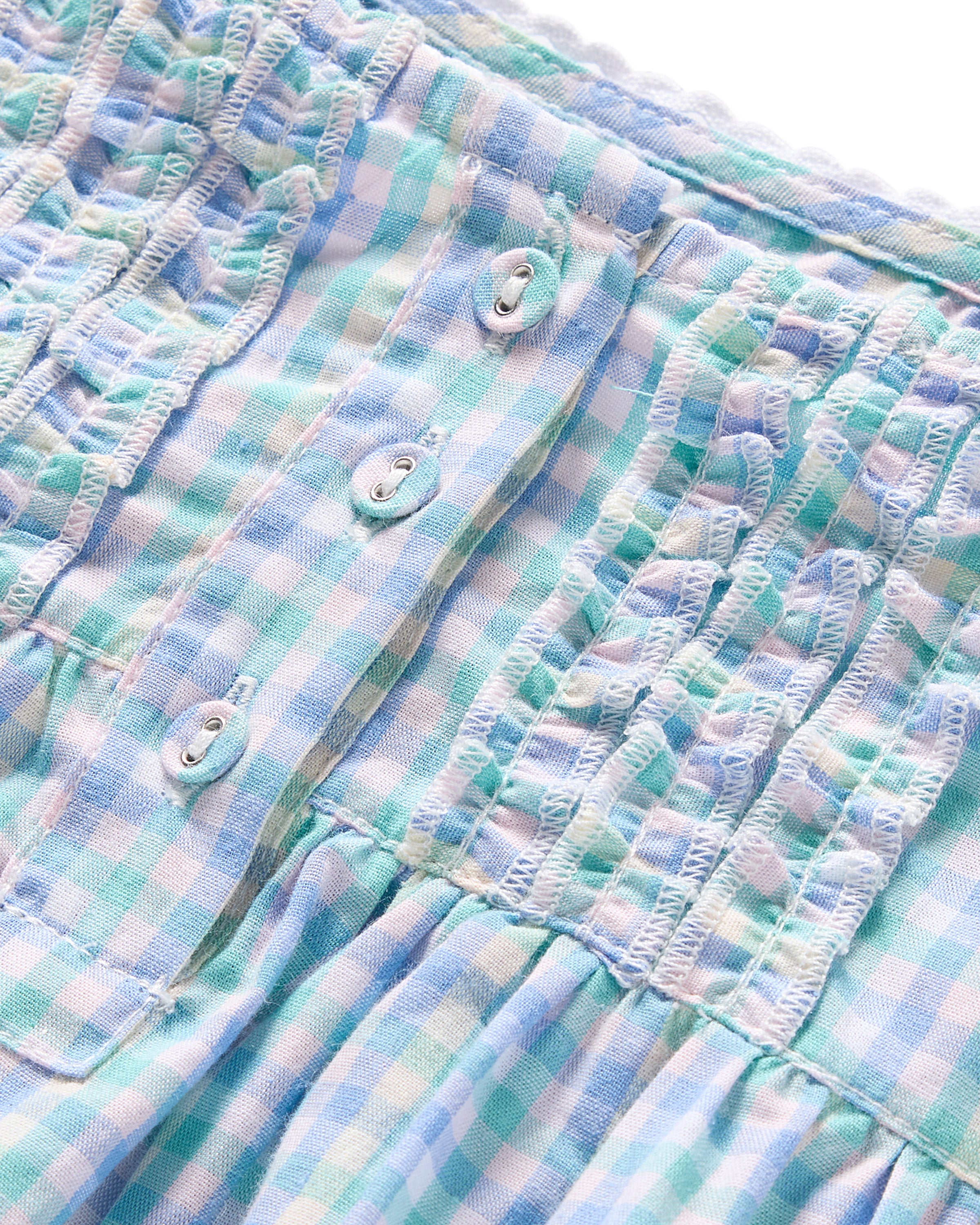Close-up of the Girls Twill Charlotte Nightgown in Spring Gingham by Petite Plume, featuring a blue and white checkered pattern. It has smocking along the top edge and a row of small white buttons, offering a textured look for breathable sleepwear.