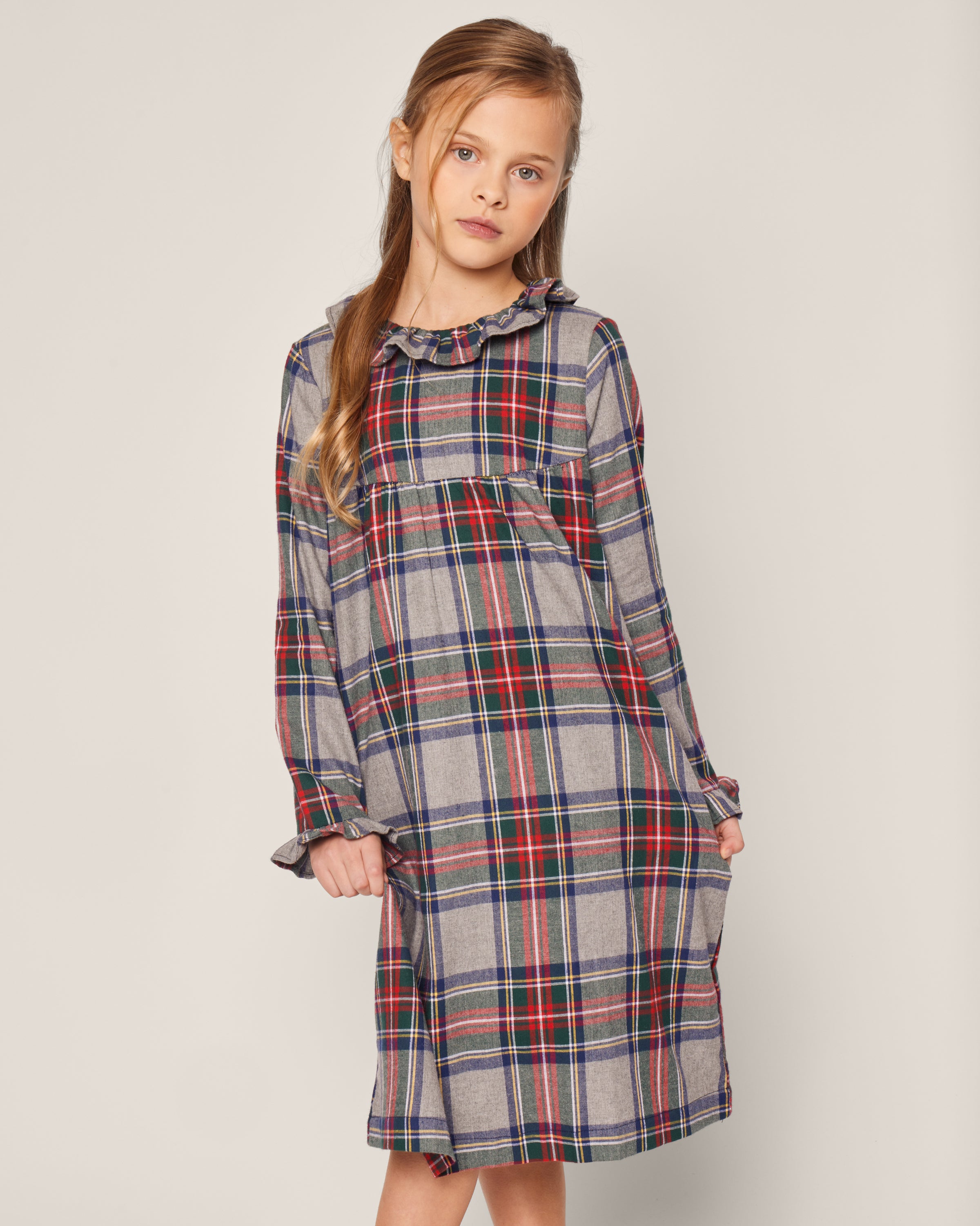 A girl in Petite Plumes Brushed Cotton Scarlett Nightgown in Westminster Tartan, featuring a ruffled collar and long sleeves. Her hair is styled in a side braid as she poses indoors against a plain background, showcasing the classic elegance of this fabric.
