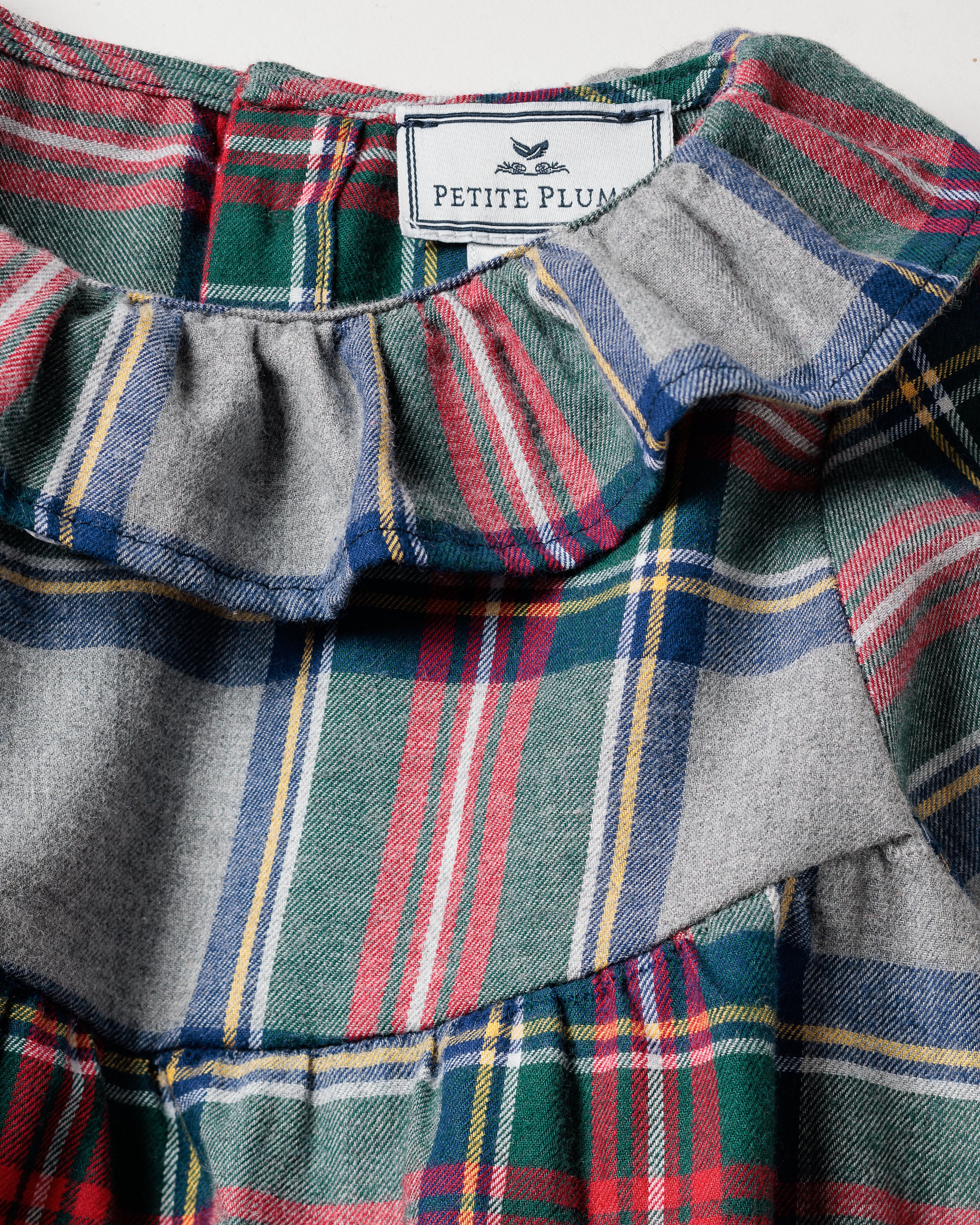 The Girls Brushed Cotton Scarlett Nightgown by Petite Plume features a close-up of Westminster Tartan with red, green, blue, and yellow stripes. The ruffled neckline adds charm to this childrens sleepwear piece, while the Petite Plume label ensures quality in its flame-retardant fabric design.
