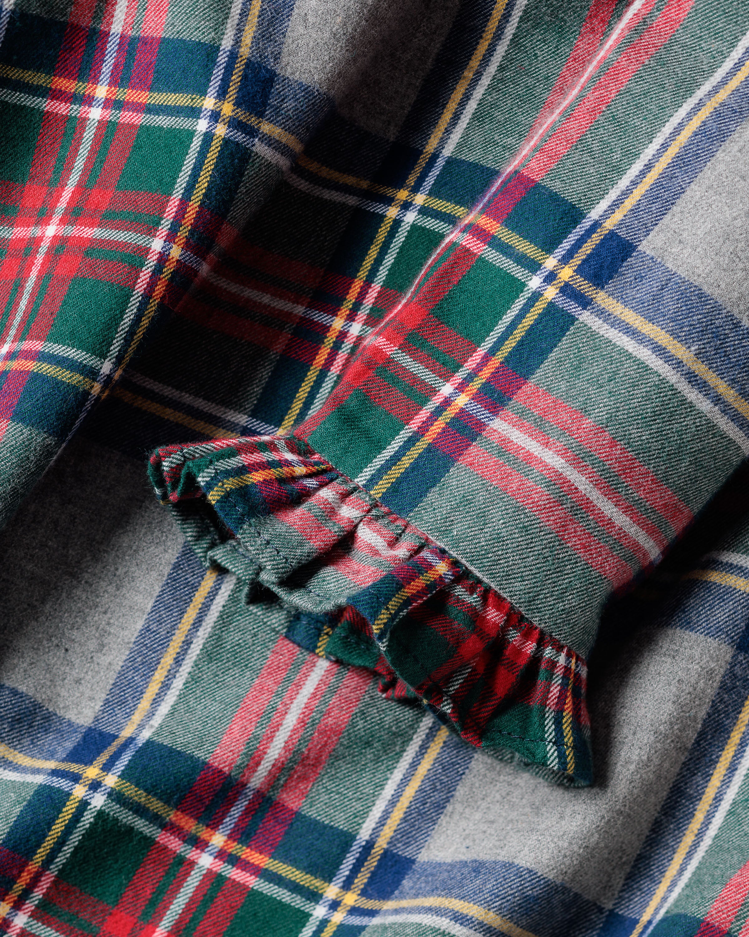 A close-up of a ruffled, flame-retardant fabric in Westminster Tartan with green, red, gray, and yellow stripes. This stylish and safe material is used in the Girls Brushed Cotton Scarlett Nightgown by Petite Plume—perfect for childrens sleepwear.