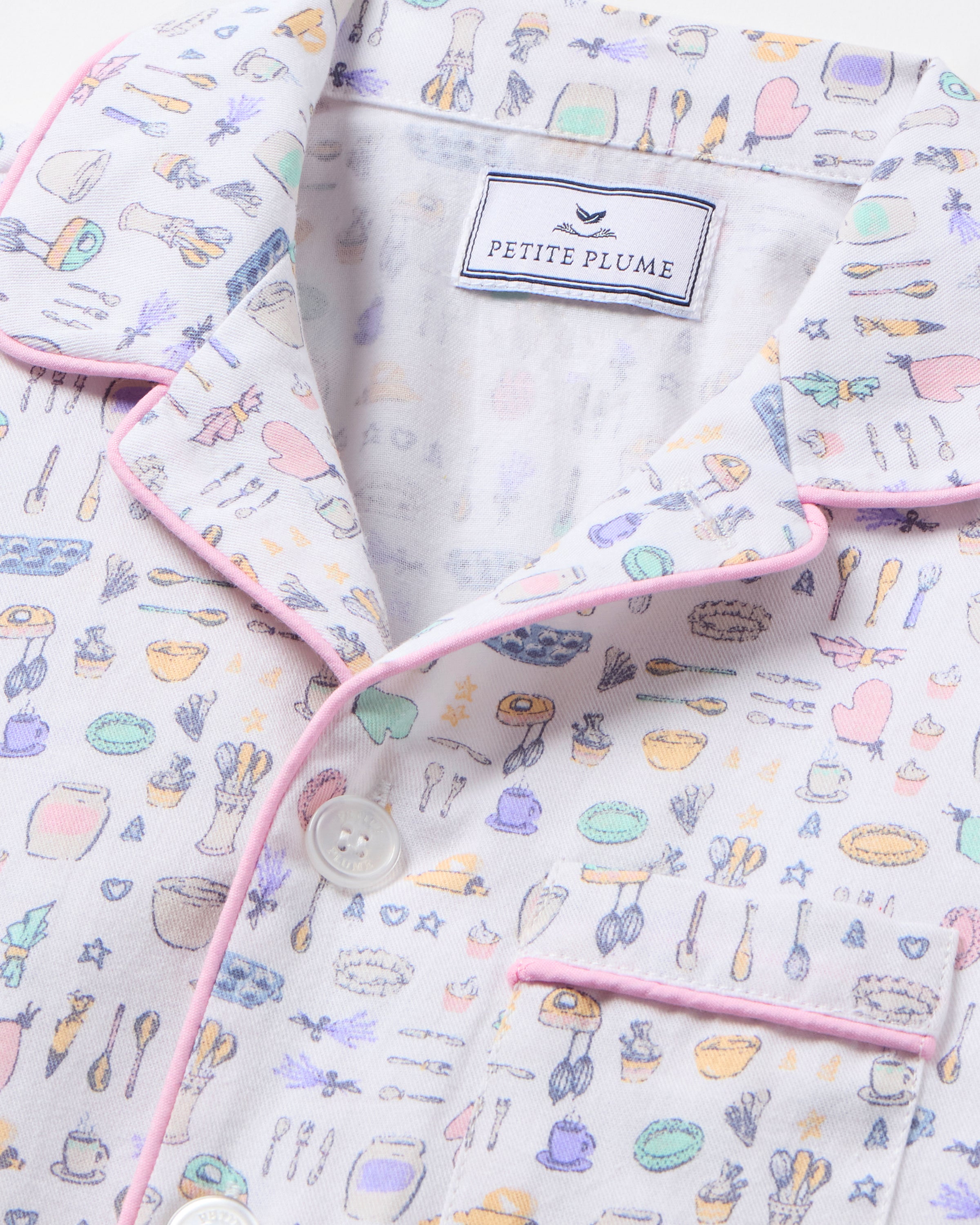 The Kid's Twill Pajama Set in Baking Spirits Bright features white long-sleeve button-up top and long pants with a colorful print of various small household and travel items.