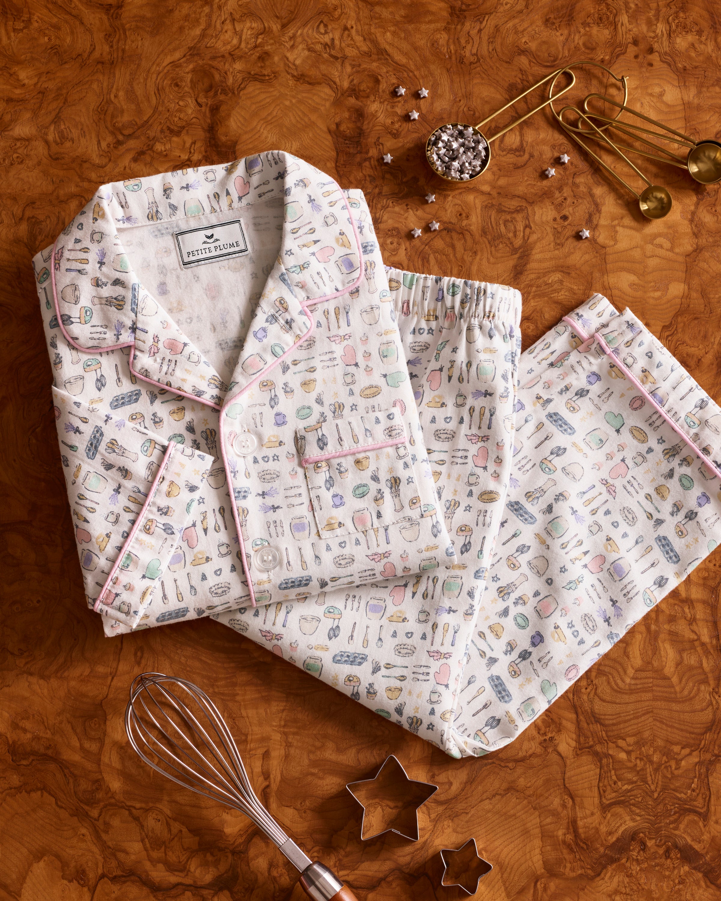 The Kid's Twill Pajama Set in Baking Spirits Bright features white long-sleeve button-up top and long pants with a colorful print of various small household and travel items.