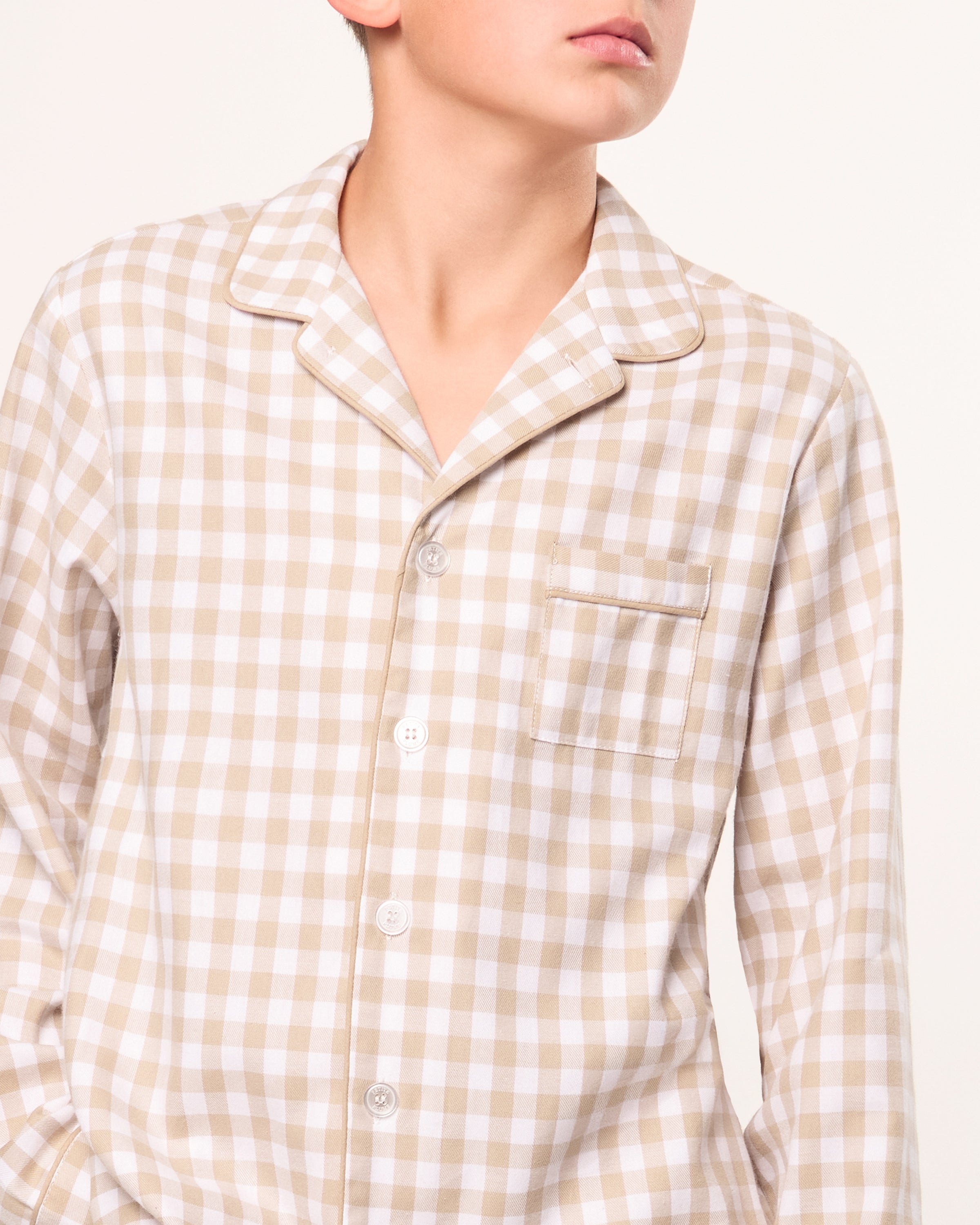 Kid's Twill Pajama Set in Camel Gingham features long sleeves, pants with an elastic waistband, and a button-up shirt with a collar and front pocket, all in a beige and white gingham check pattern.