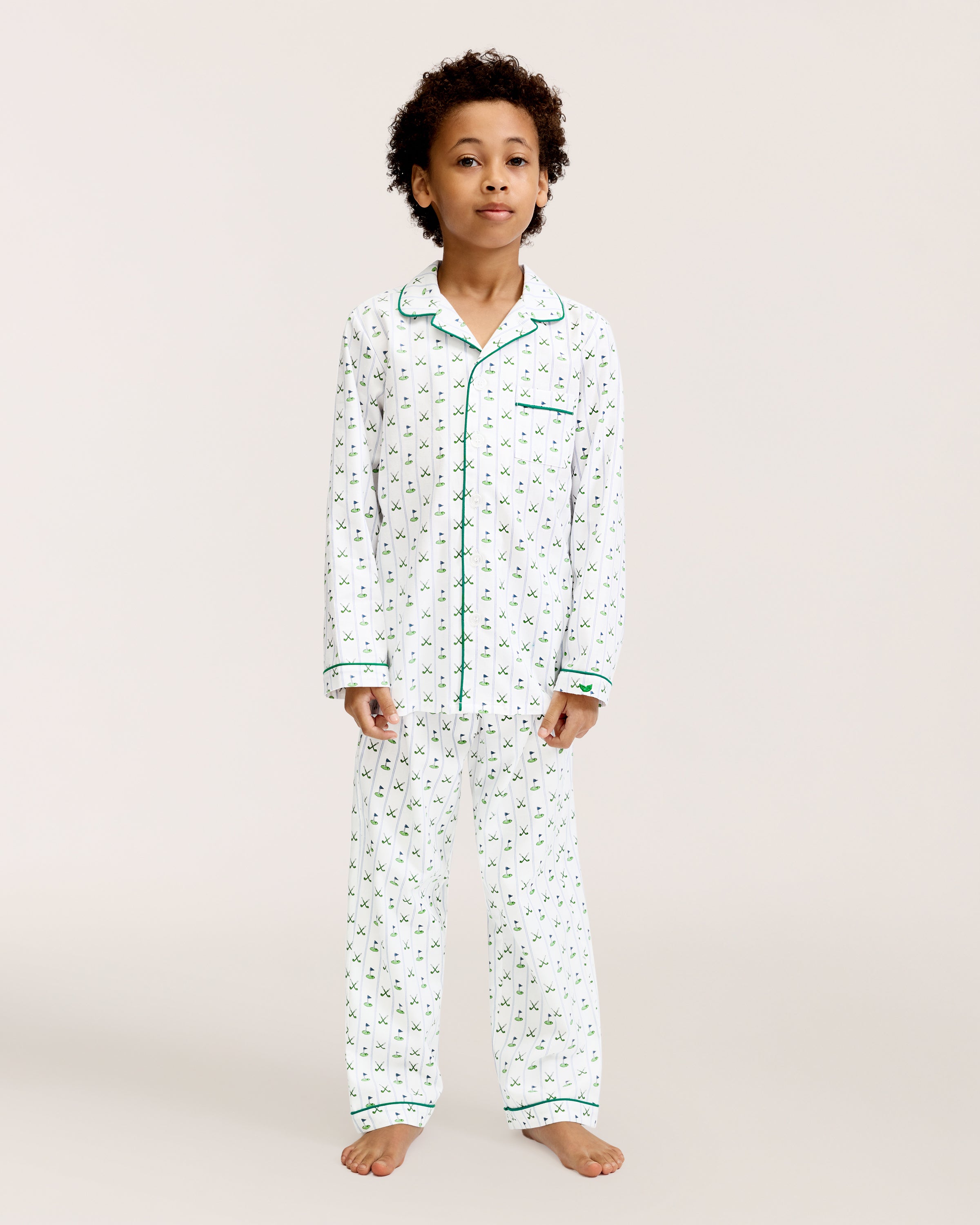 The Kid's Twill Pajama Set in Fairway Stripe features white pajamas with green piping, a tennis racket and green stripe pattern, a long-sleeve button-up top with a chest pocket, and matching long pants.