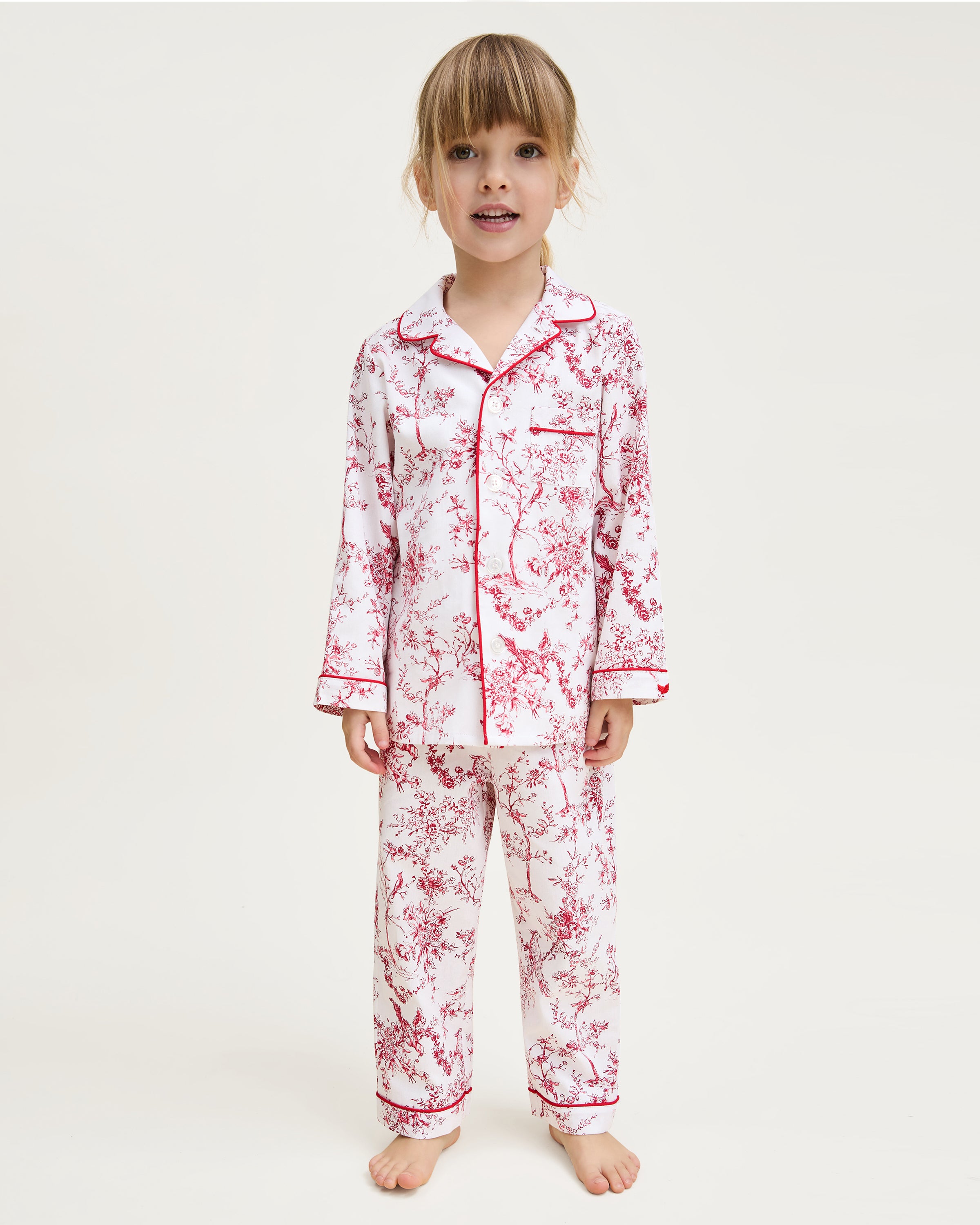 The Kid's Twill Pajama Set in Red Timeless Toile features a white base with red toile print, long-sleeve button-up top with front pocket, matching pants, and red piping accents.
