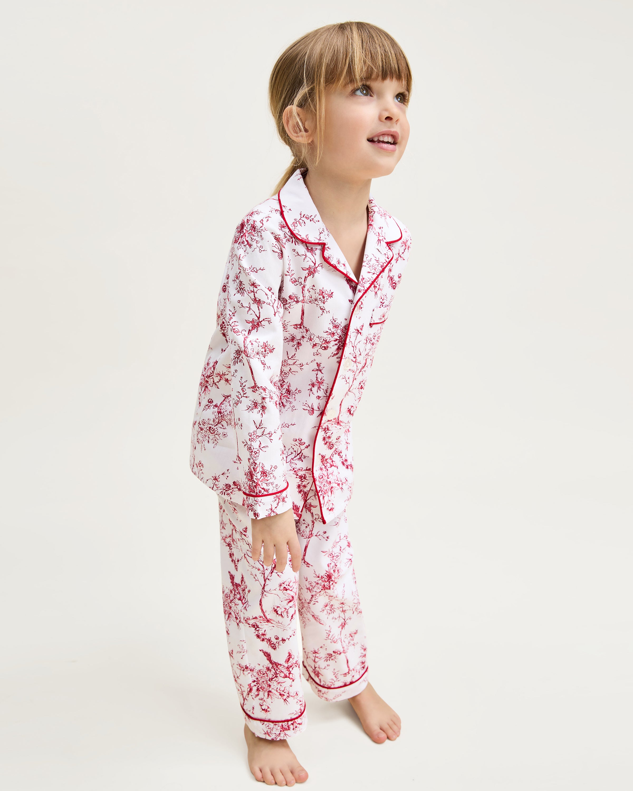 The Kid's Twill Pajama Set in Red Timeless Toile features a white base with red toile print, long-sleeve button-up top with front pocket, matching pants, and red piping accents.