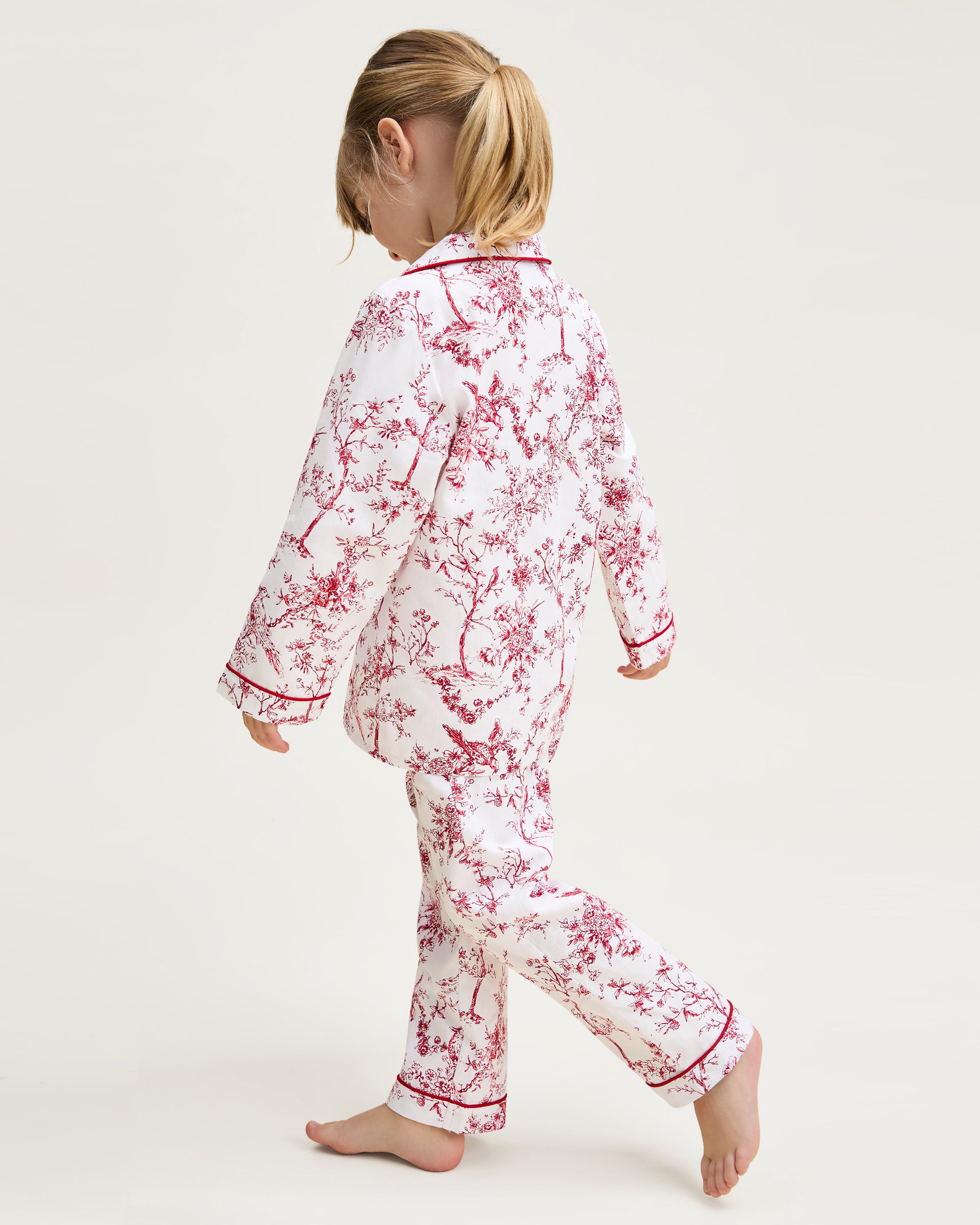 The Kid's Twill Pajama Set in Red Timeless Toile features a white base with red toile print, long-sleeve button-up top with front pocket, matching pants, and red piping accents.