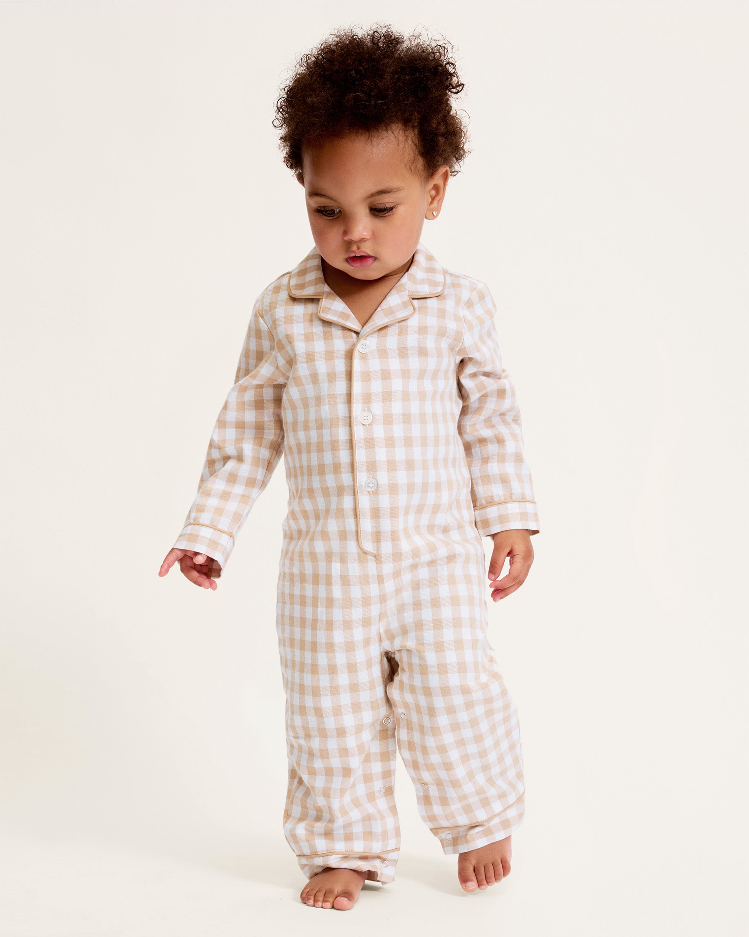 The Baby's Twill Classic Romper in Camel Gingham features long sleeves, a beige and white gingham check pattern, front buttons, snap closures at the legs, a collar, and cuffed sleeves and legs.