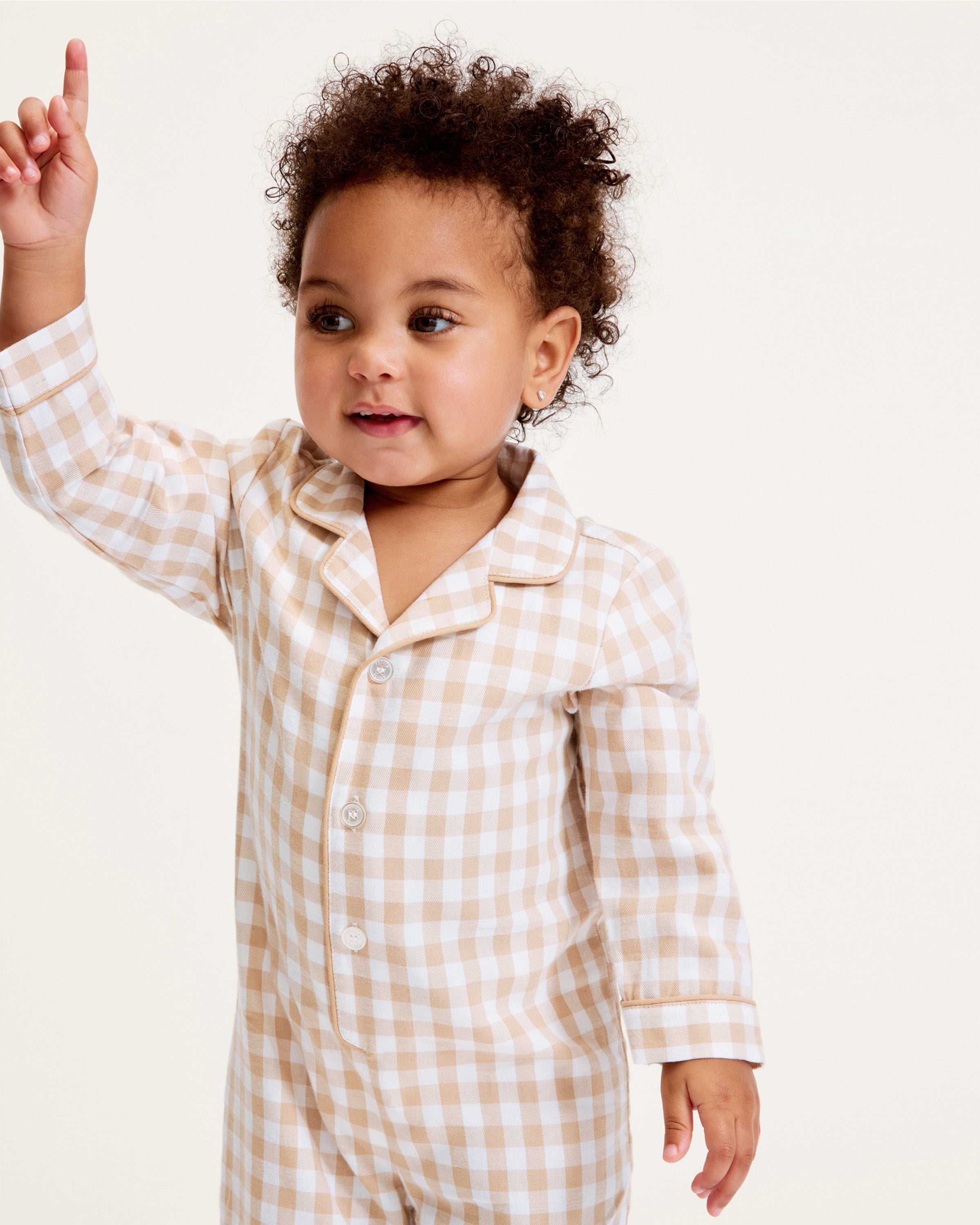 The Baby's Twill Classic Romper in Camel Gingham features long sleeves, a beige and white gingham check pattern, front buttons, snap closures at the legs, a collar, and cuffed sleeves and legs.