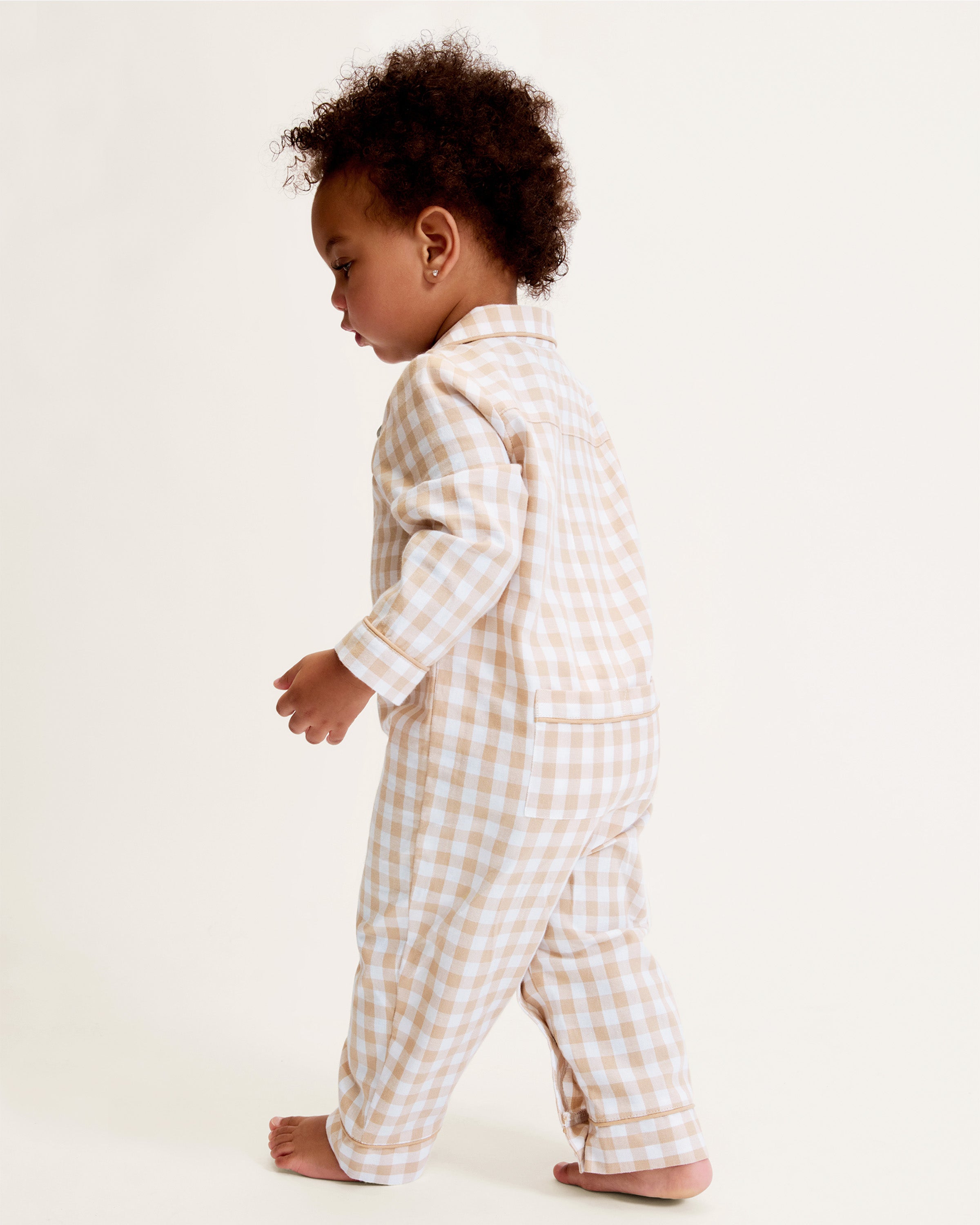 The Baby's Twill Classic Romper in Camel Gingham features long sleeves, a beige and white gingham check pattern, front buttons, snap closures at the legs, a collar, and cuffed sleeves and legs.