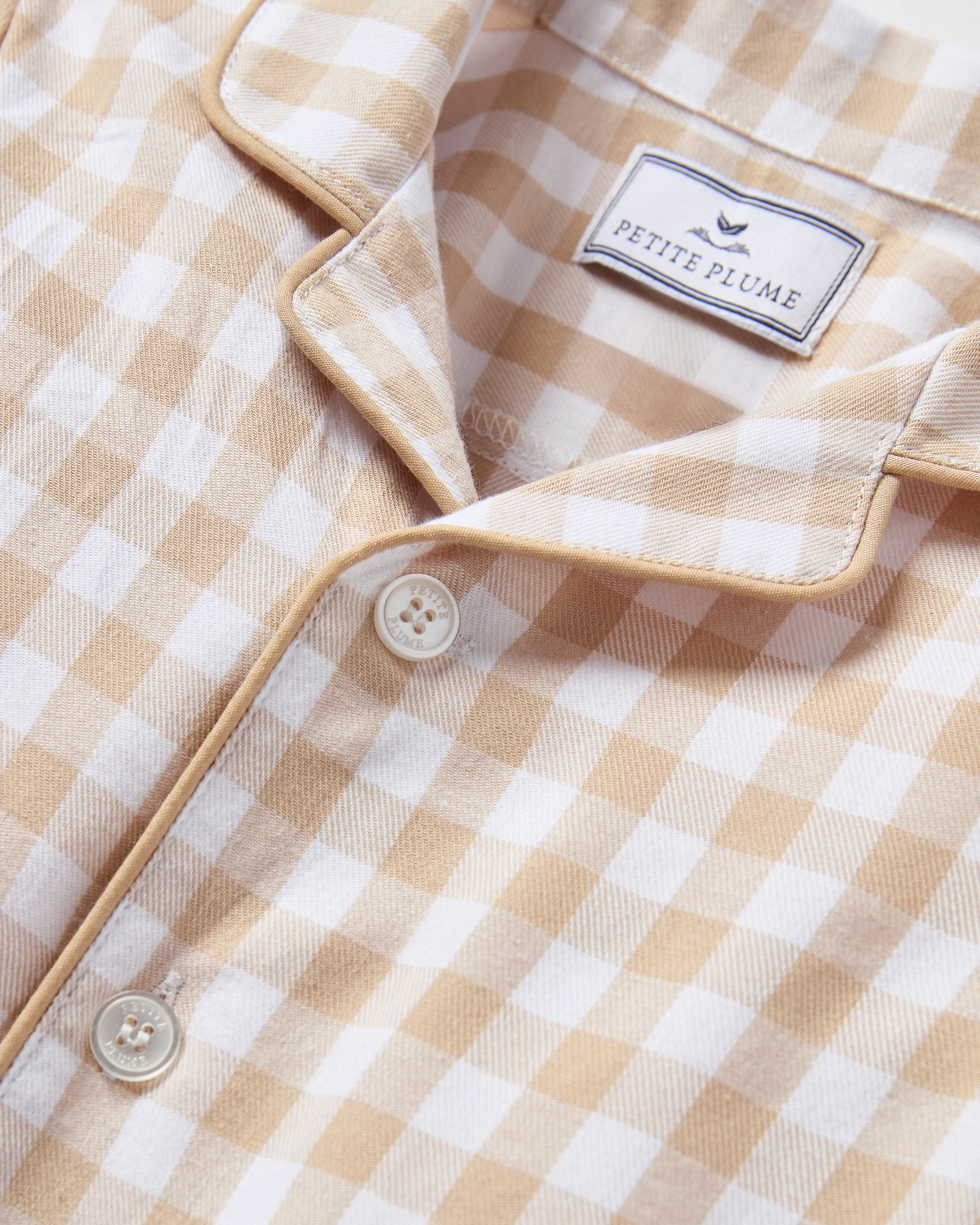 The Baby's Twill Classic Romper in Camel Gingham features long sleeves, a beige and white gingham check pattern, front buttons, snap closures at the legs, a collar, and cuffed sleeves and legs.