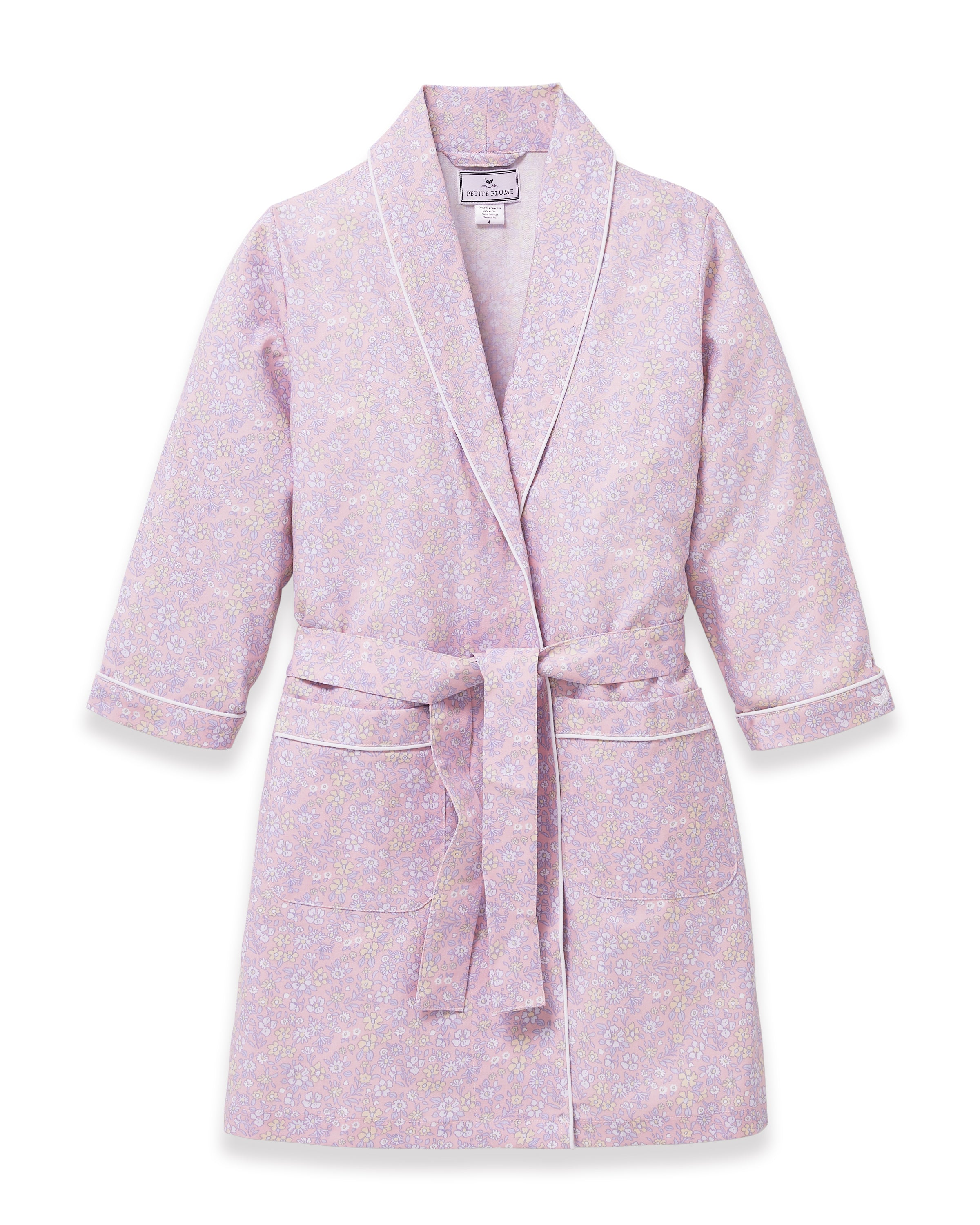 A young girl with blonde hair smiles as she ties the belt on her Kid's Twill Robe in Fleur Blush over a white nightgown.