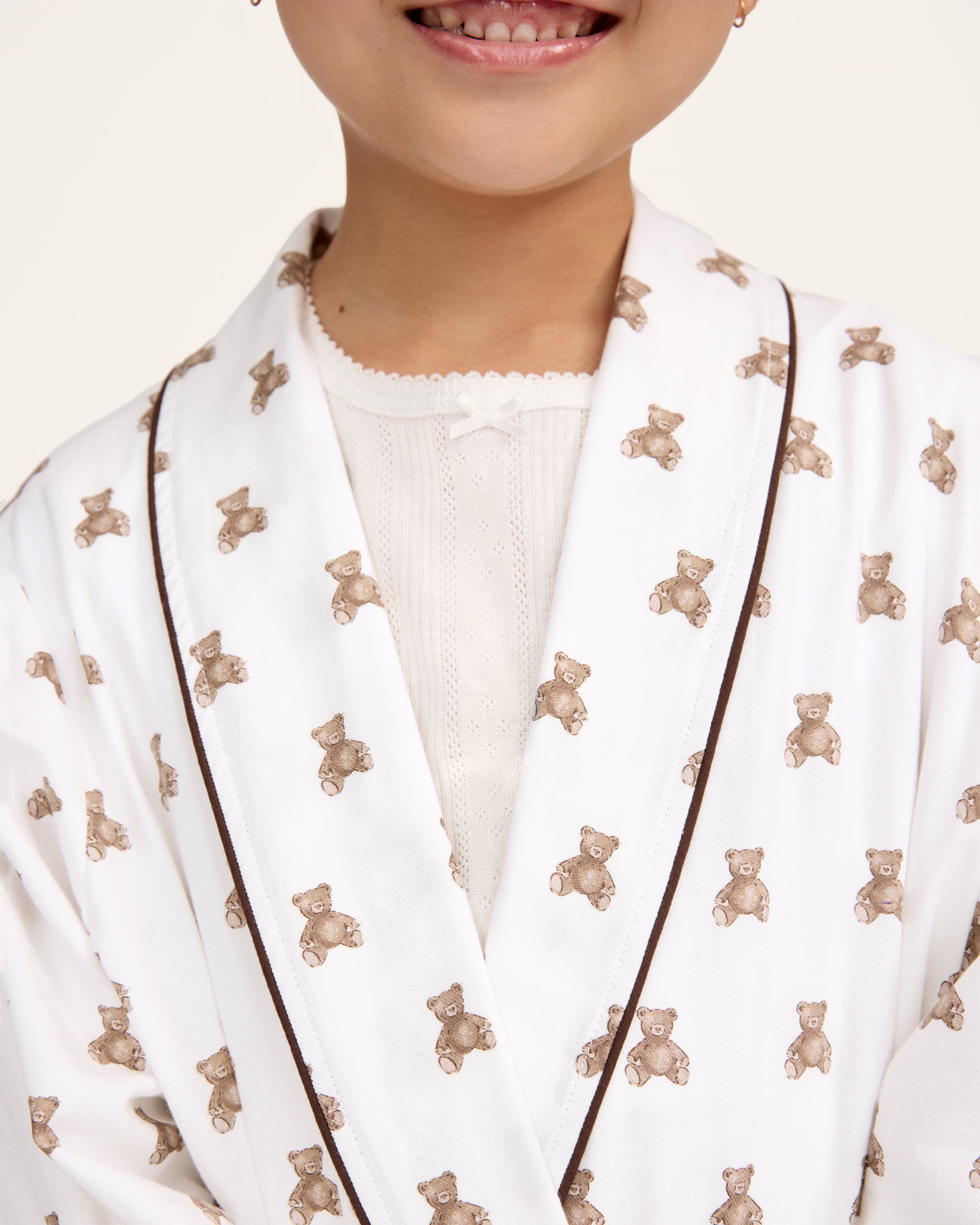 The Kid's Brushed Twill Robe in Teddy Tales features a white base with brown bear prints, black piping, two front pockets, and a matching waist belt.