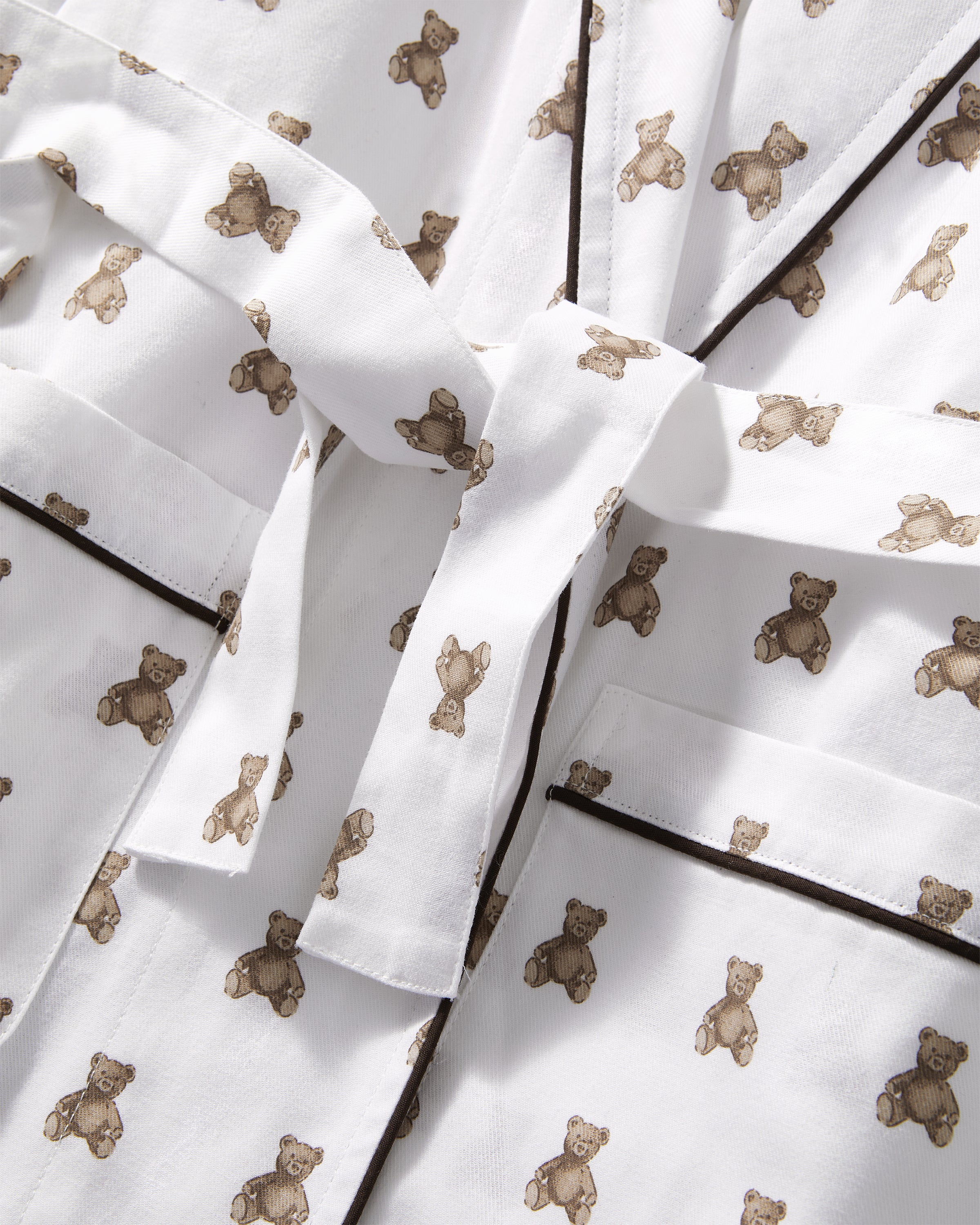 The Kid's Brushed Twill Robe in Teddy Tales features a white base with brown bear prints, black piping, two front pockets, and a matching waist belt.