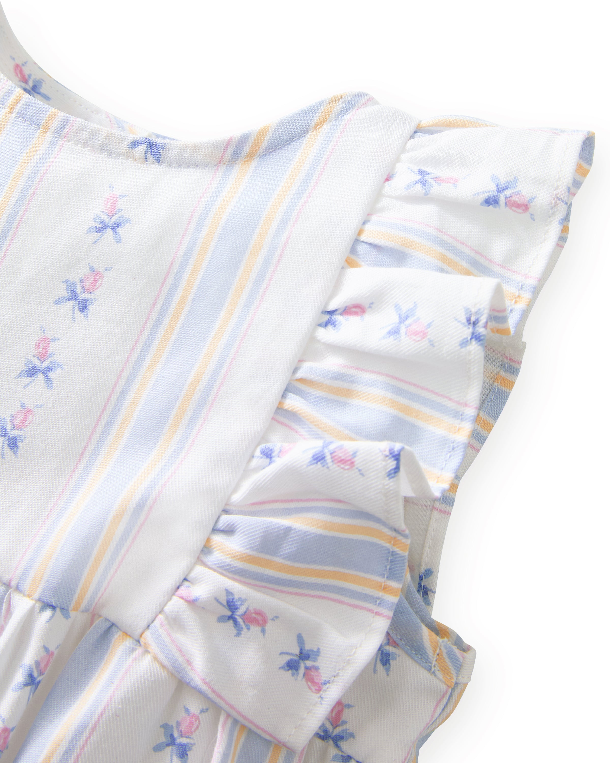 A smiling toddler with curly hair stands barefoot against a plain white background, wearing the Baby's Twill Ruffled Romper in Cottage Stripe—featuring pastel stripes, small floral patterns, and ruffled sleeves.