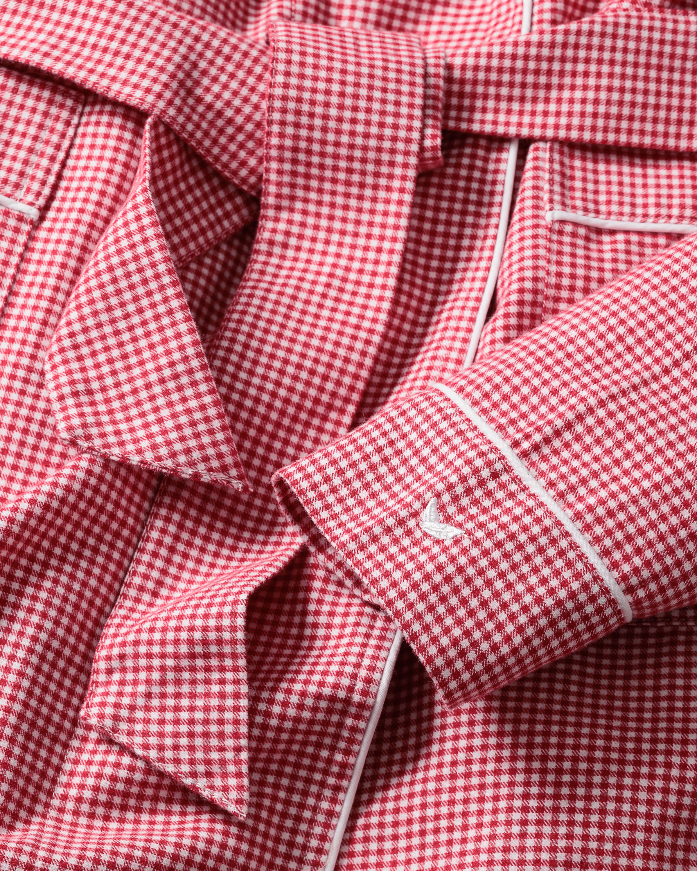 Close-up of a red mini gingham print fabric with a belt and cuff featuring a small embroidered logo, likely from Petite Plumes Kids Flannel Robe. The garment has visible white piping along its edges.
