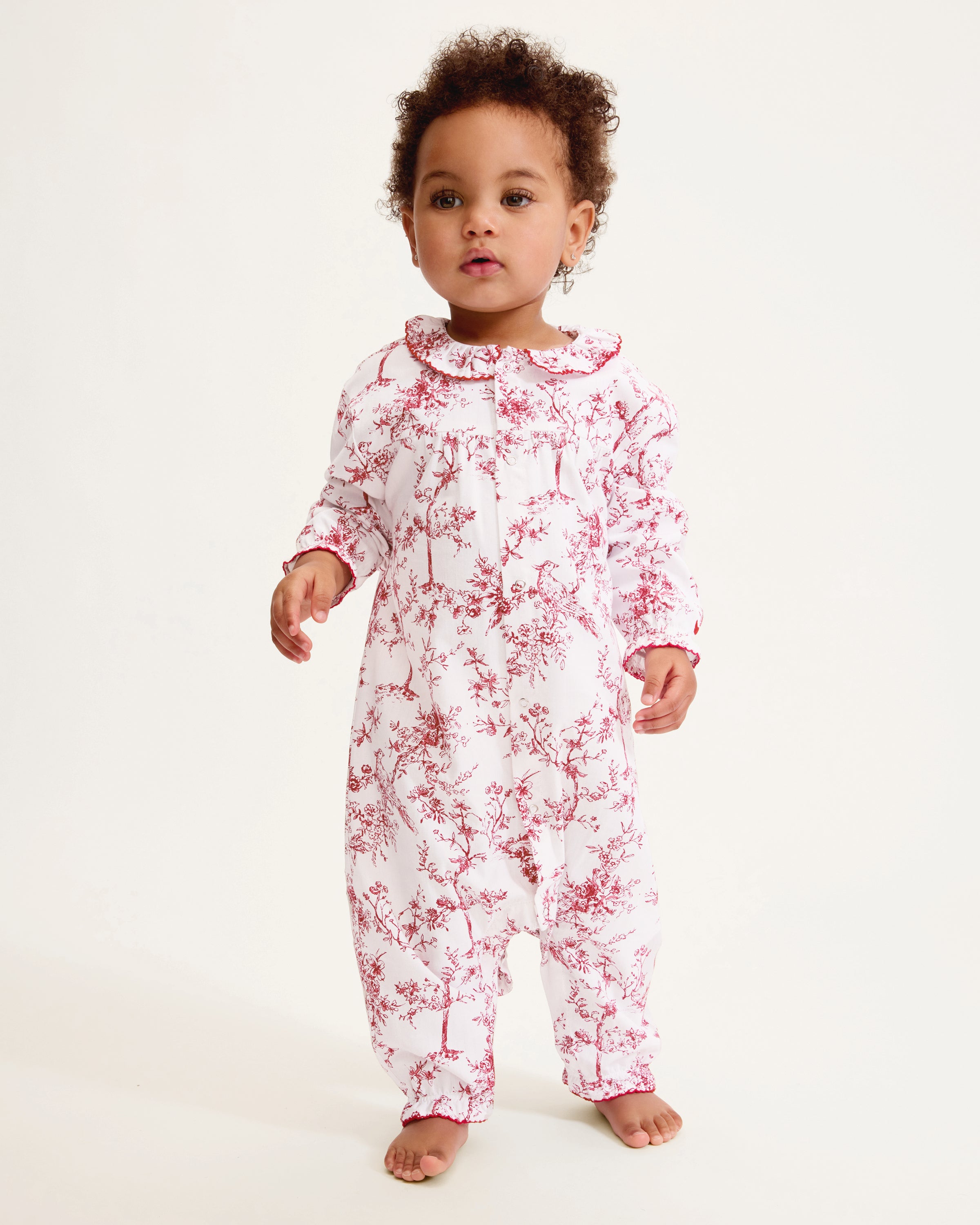The Baby's Twill Madeline Romper in Red Timeless Toile features long sleeves, a ruffled collar, red floral print, and snap buttons down the front and legs.