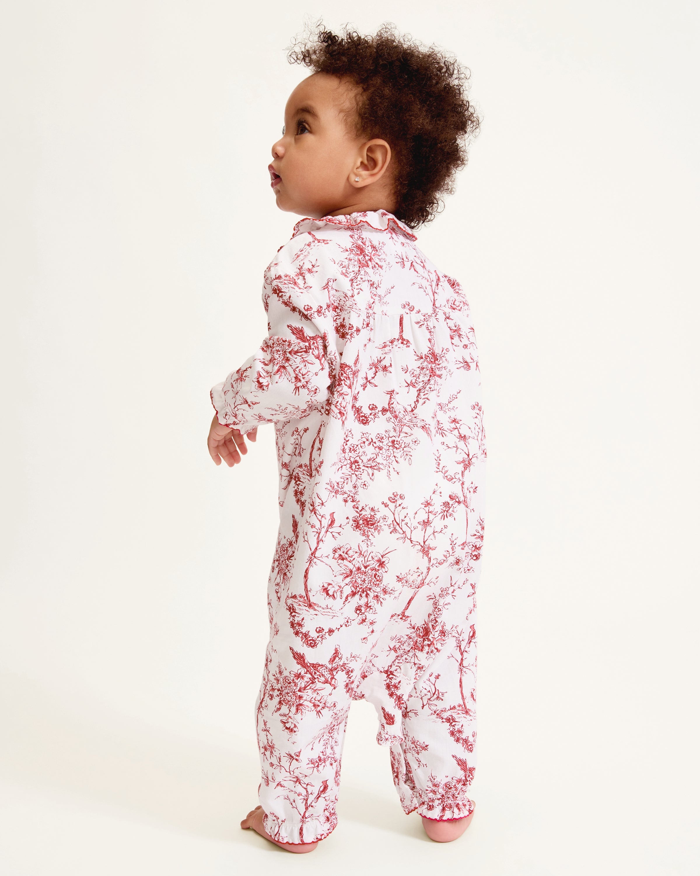 The Baby's Twill Madeline Romper in Red Timeless Toile features long sleeves, a ruffled collar, red floral print, and snap buttons down the front and legs.