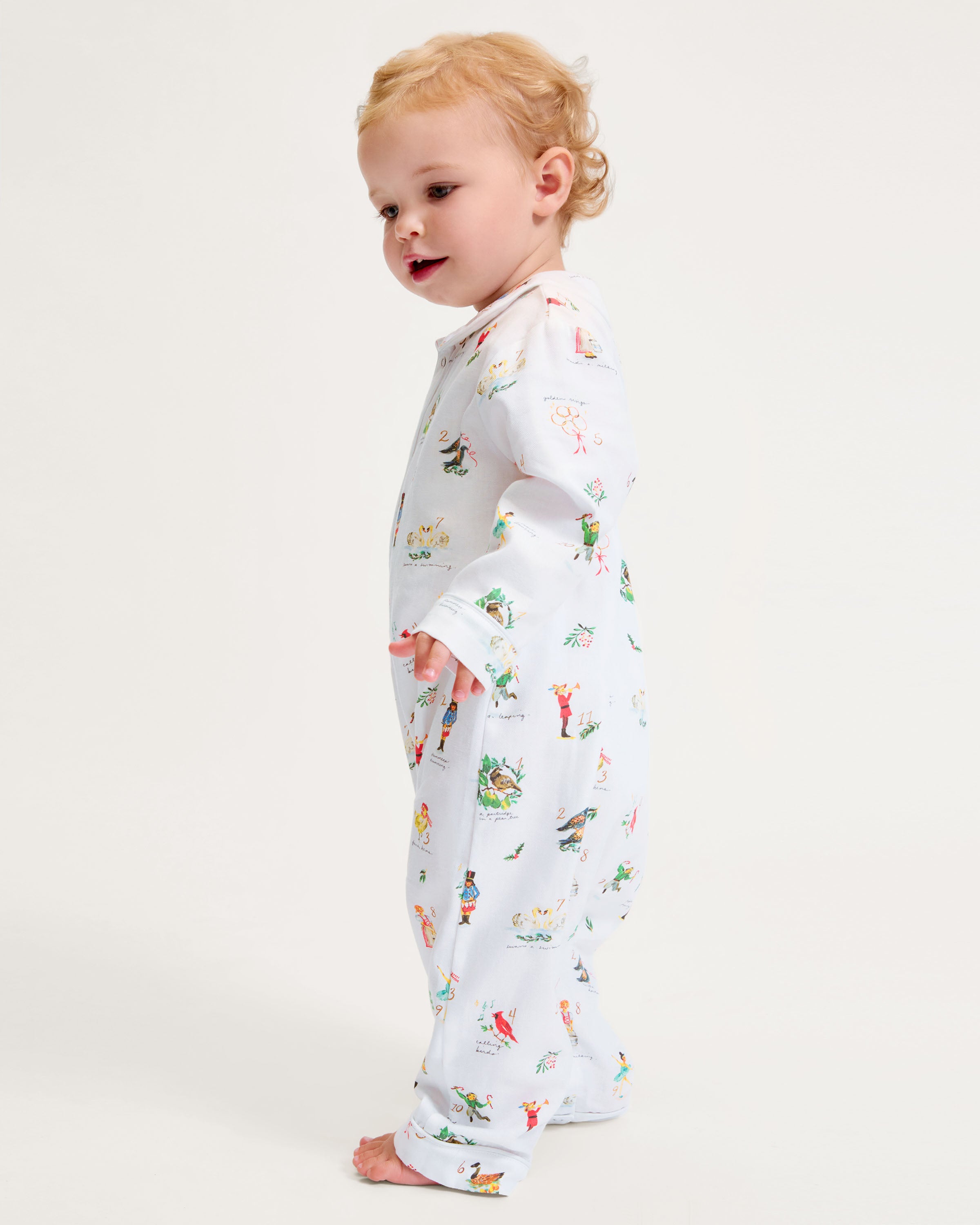 The Baby's Twill Cambridge Romper in 12 Days of Christmas features a white long-sleeve design with a collar, playful festive illustrations, and convenient snap buttons down the front and legs.