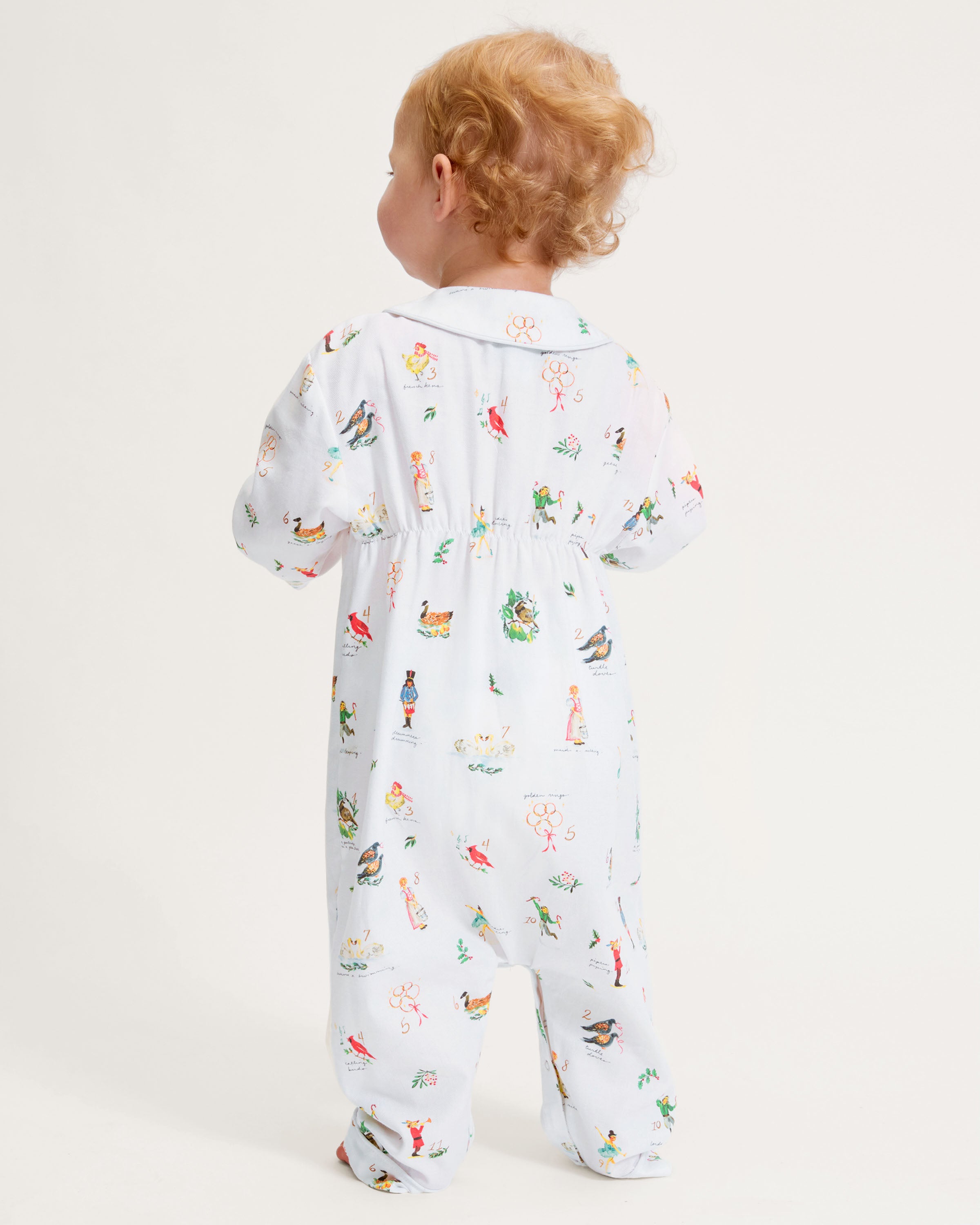 The Baby's Twill Cambridge Romper in 12 Days of Christmas features a white long-sleeve design with a collar, playful festive illustrations, and convenient snap buttons down the front and legs.
