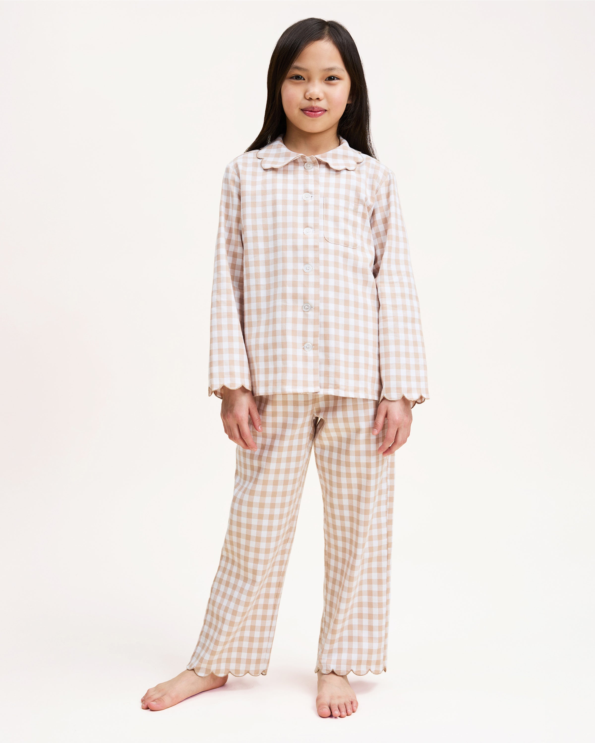 Kid's Twill Colette Pajama Set in Camel Gingham, featuring a beige and white gingham pattern with a scalloped collar, long sleeves, front pocket, and matching elastic-waist pants, is displayed neatly on a white background.