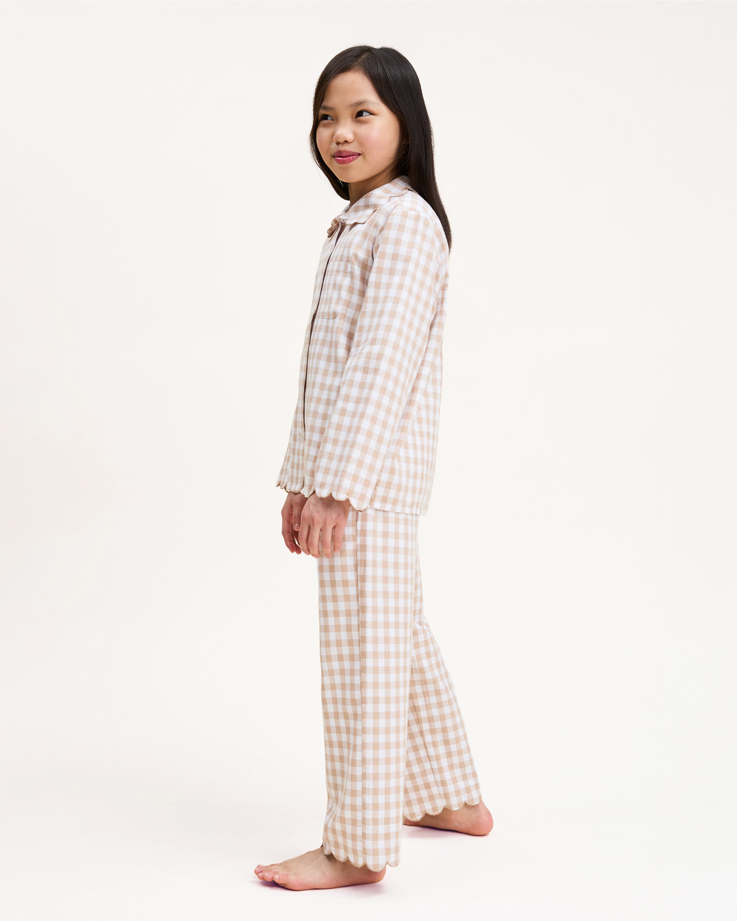 Kid's Twill Colette Pajama Set in Camel Gingham, featuring a beige and white gingham pattern with a scalloped collar, long sleeves, front pocket, and matching elastic-waist pants, is displayed neatly on a white background.