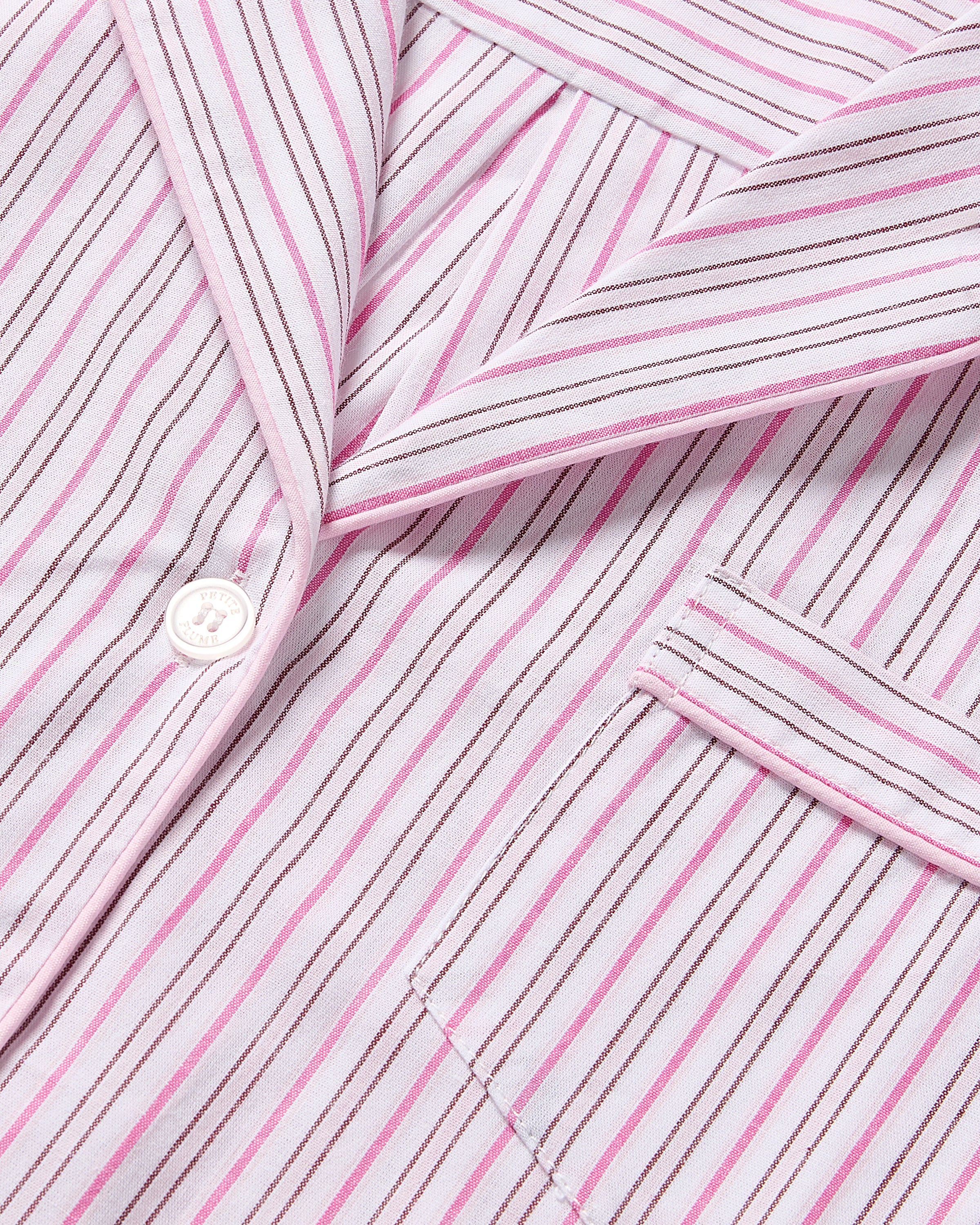 The Kids Twill Short Set in Blush Boulevard by Petite Plume is a collared shirt with a pink and white striped design, ideal for Valentines Day sleepwear. It includes button fastening and a front pocket, crafted from luxurious cotton with delicate pink piping along the collar and pocket edges.