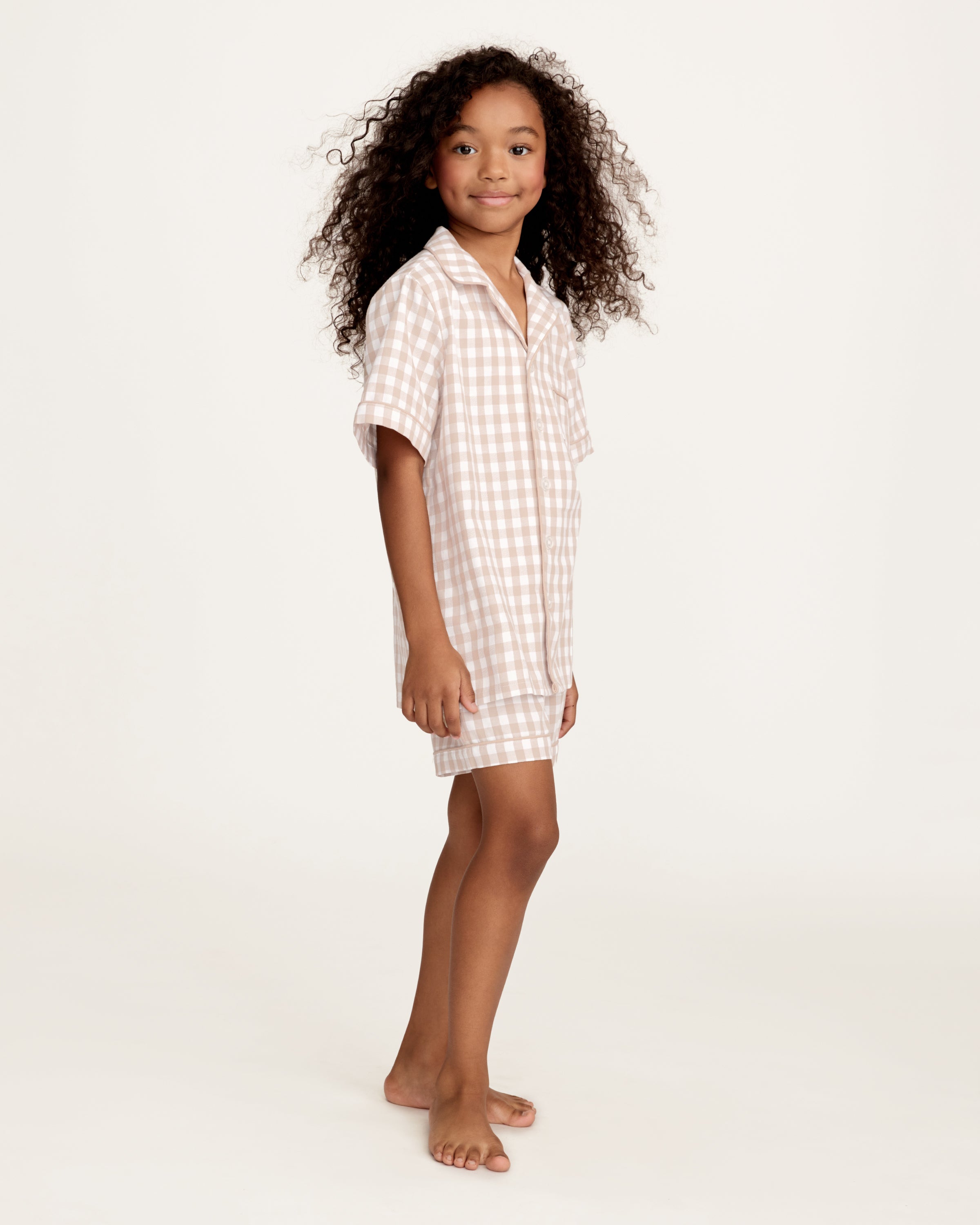 The Kid's Twill Pajama Short Set in Camel Gingham features a light beige and white gingham pattern with a collared, button-front top, chest pocket, and elastic waist shorts.