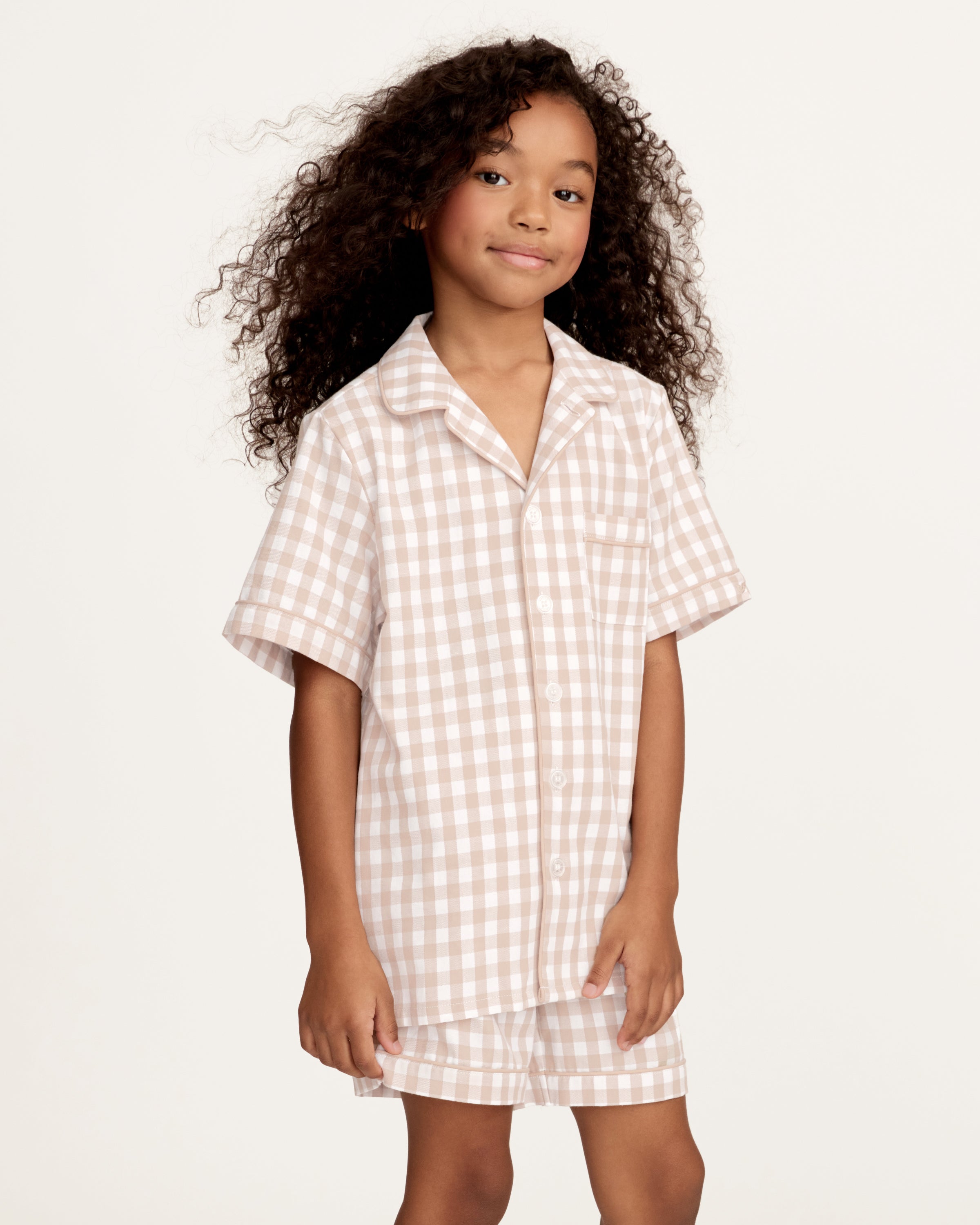 The Kid's Twill Pajama Short Set in Camel Gingham features a light beige and white gingham pattern with a collared, button-front top, chest pocket, and elastic waist shorts.
