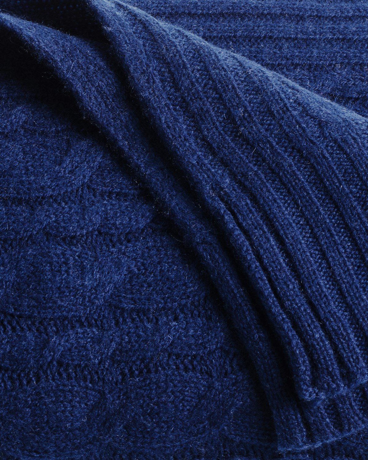 The Petite Plume Cashmere Cable Knit Throw in Navy showcases a textured cable-knit pattern and ribbed edges for a luxurious touch to your decor.