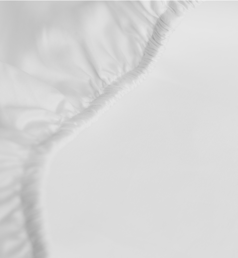 Close-up of a white fitted bed sheet showing its elastic edge and smooth fabric, with soft lighting creating a clean, minimal, and slightly abstract appearance.